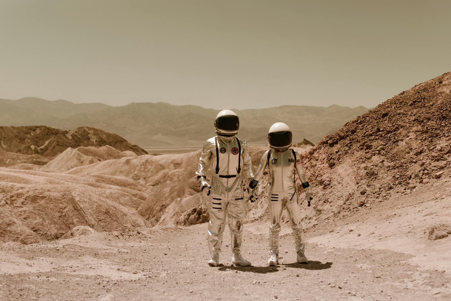 Two astronauts hold hands in a barren desert landscape, evoking a space exploration theme.