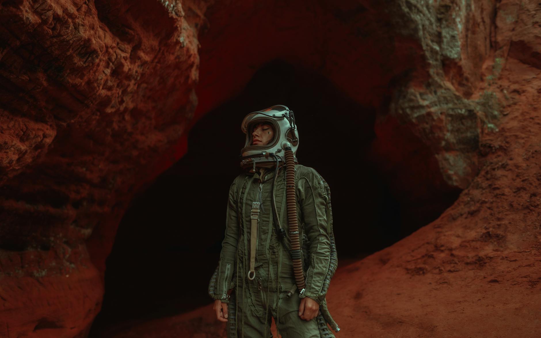 Astronaut in helmet explores a rugged, red-hued cave, exuding adventure and mystery.
