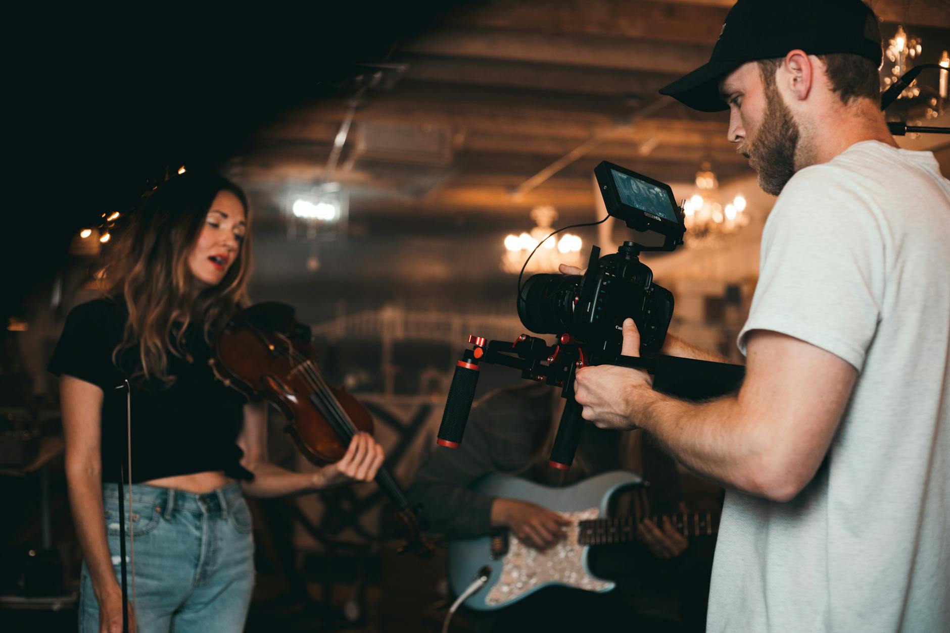 Filmmaker capturing a musician playing violin during an indoor music video shoot.