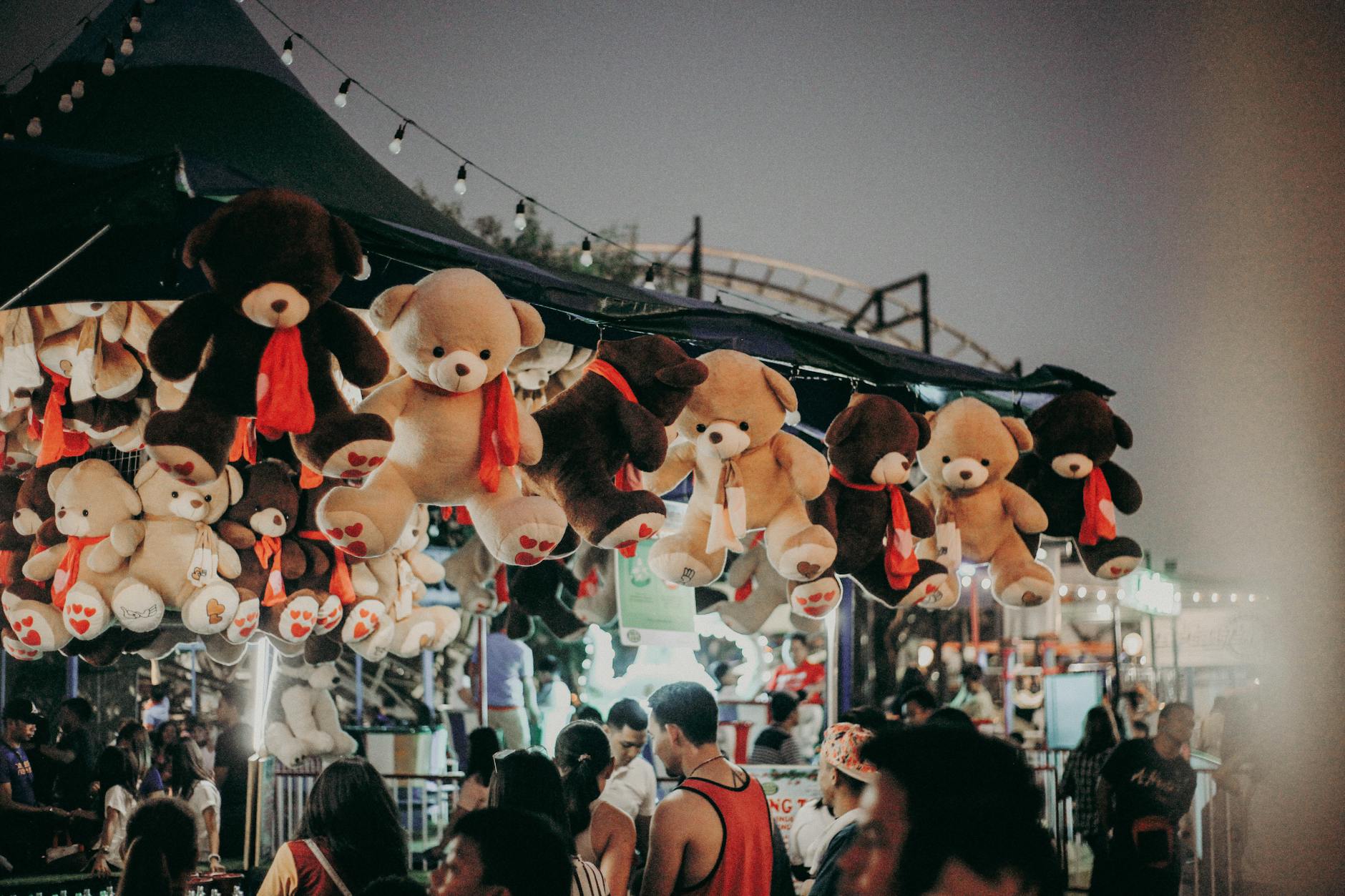 A bustling carnival scene at night featuring teddy bear prizes and a lively crowd.
