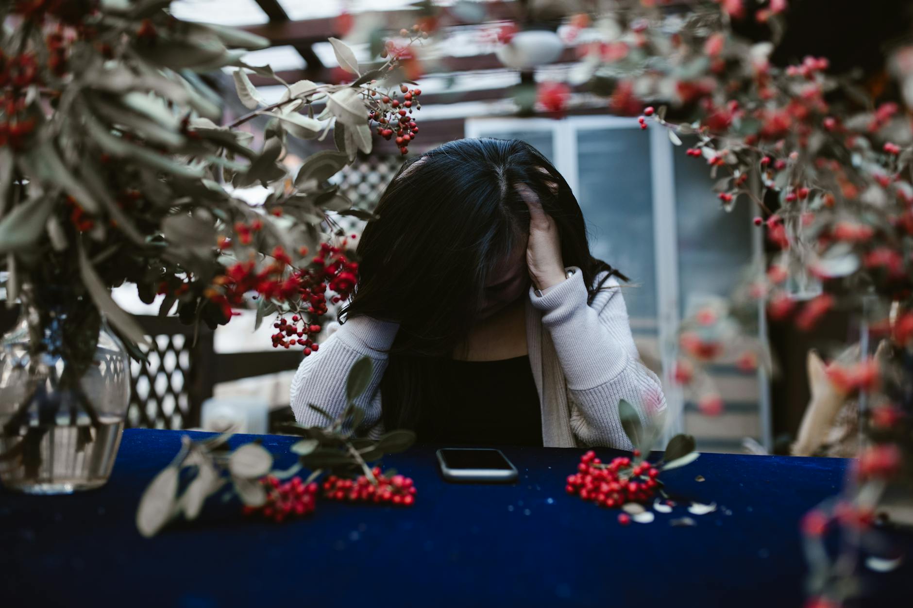 Woman in despair at table with red berries and smartphone, hands on head.