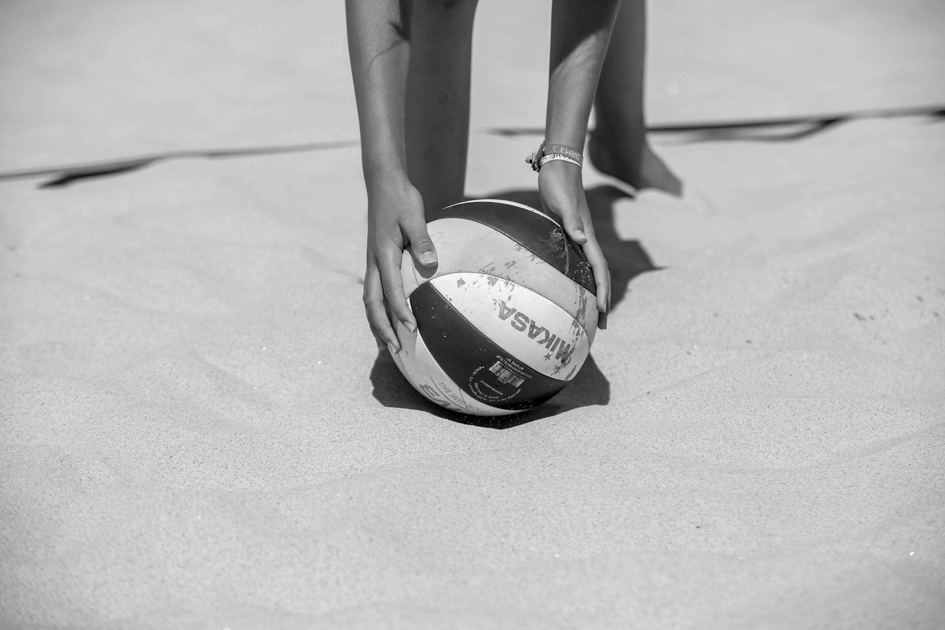 Close-up of a volleyball being placed on the beach sand in black and white.