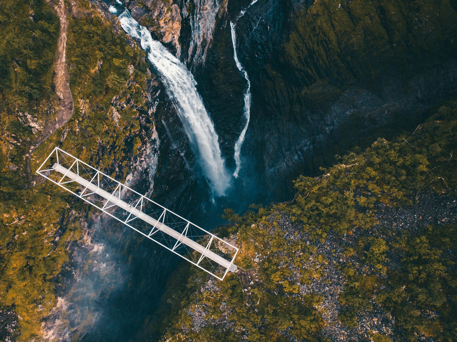 A breathtaking view of a waterfall beneath a bridge in Norway's rugged landscape captured from above.