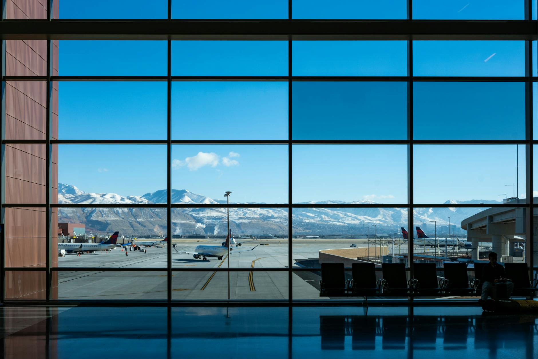 Panoramic view of airport terminal and runway with snow-capped mountains in the background.
