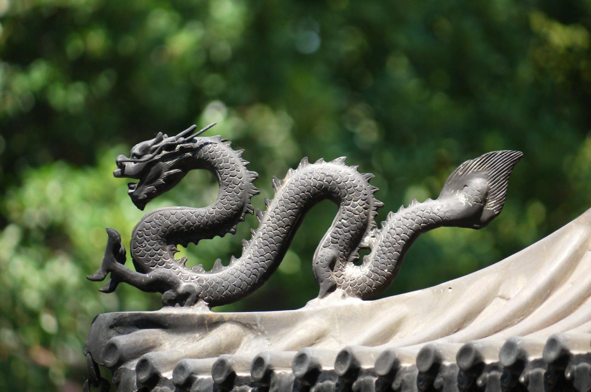 Decorative dragon sculpture on a traditional roof with a blurred natural background.