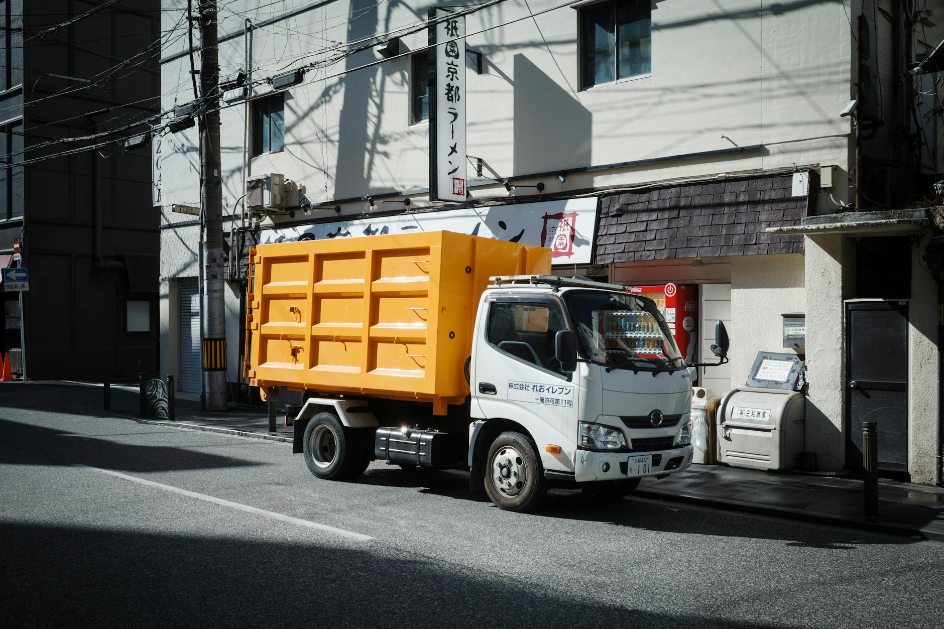 Bright yellow garbage truck parked on an urban street in Kyoto, Japan, with surrounding city buildings.