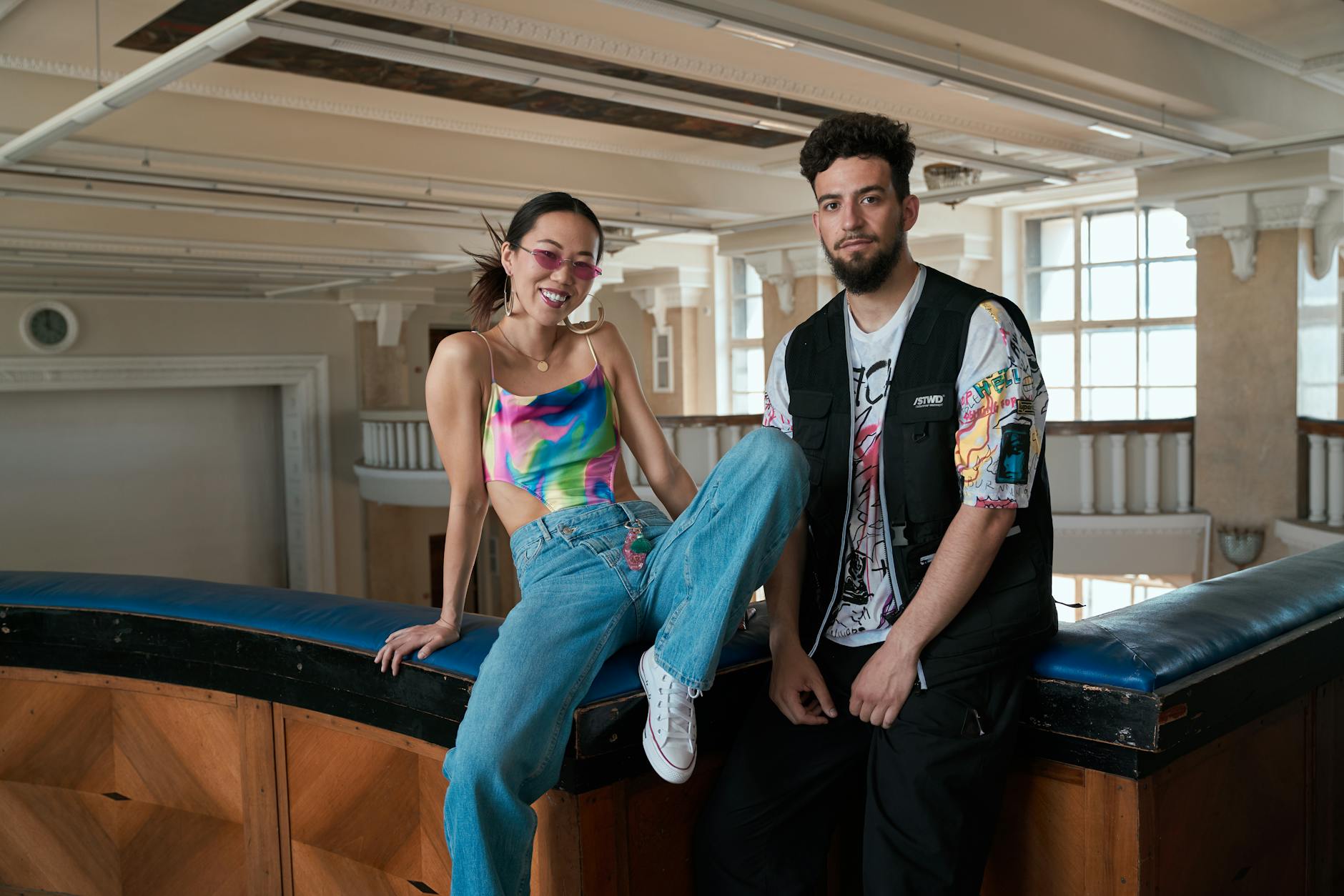 Trendy interracial couple posing in vibrant streetwear indoors, showcasing modern urban fashion.