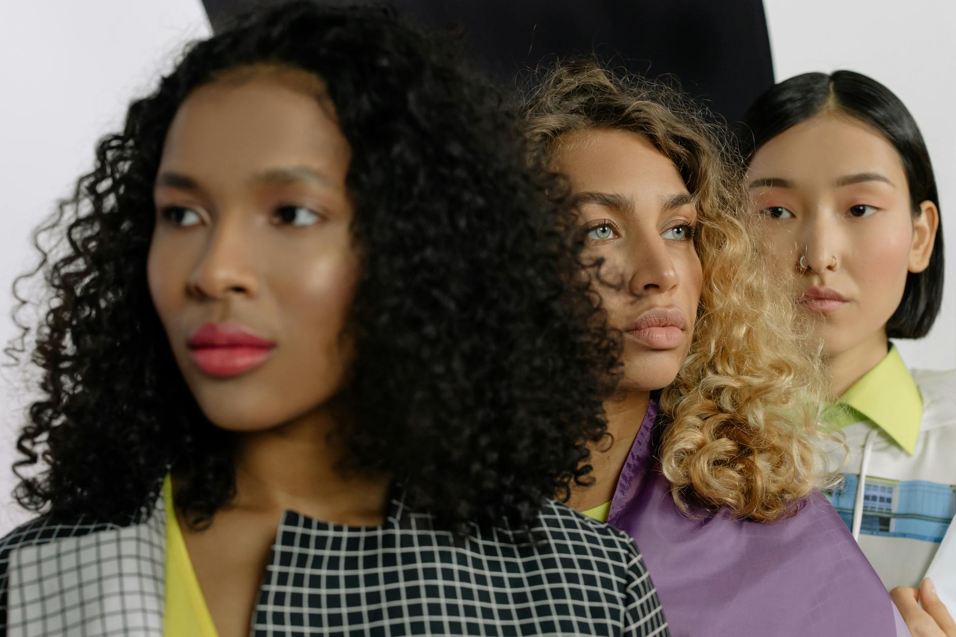 Three stylish women posing together in a studio setting emphasizing diversity and modern fashion.