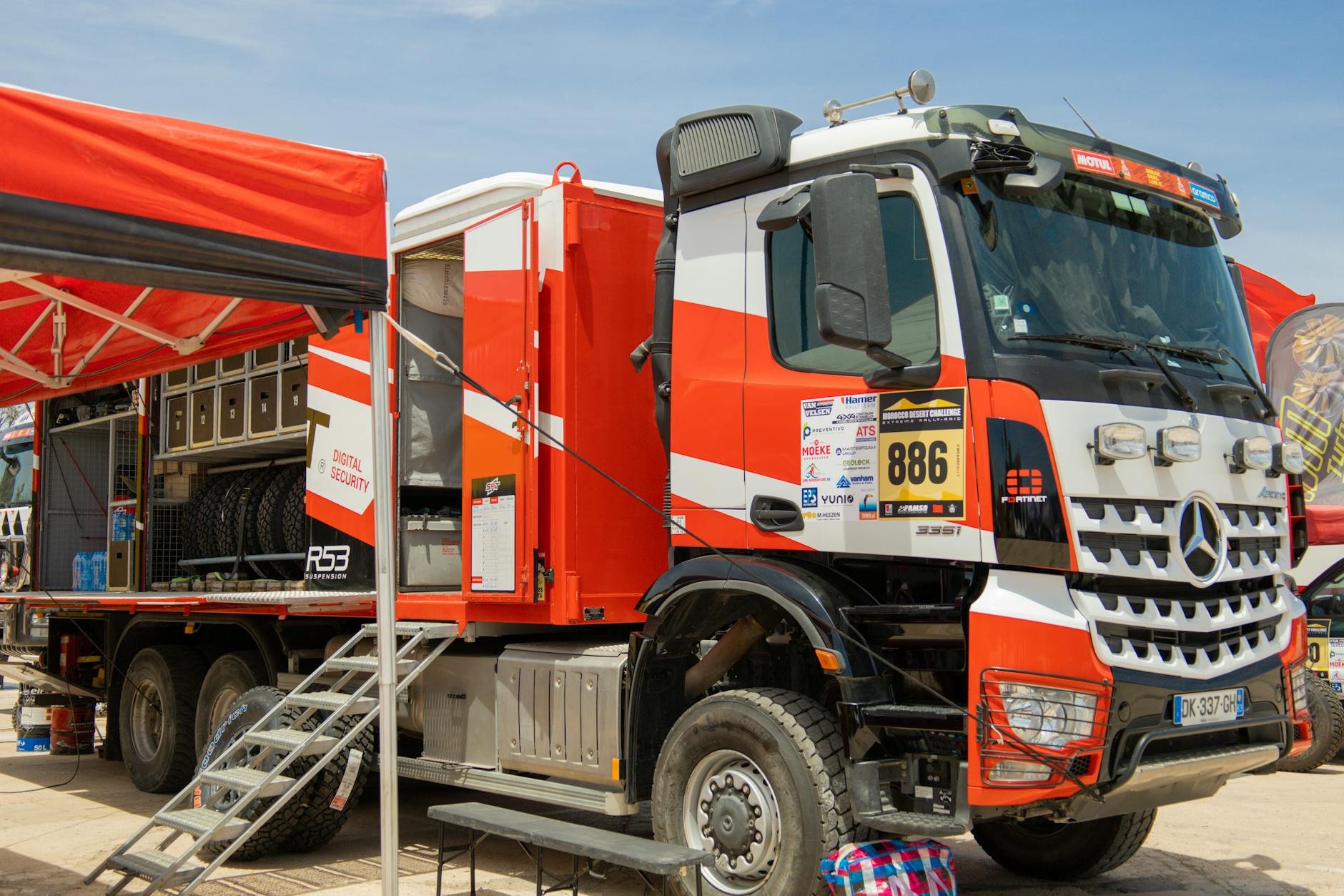 Heavy-duty rally truck prepared for off-road competition, parked under a canopy.