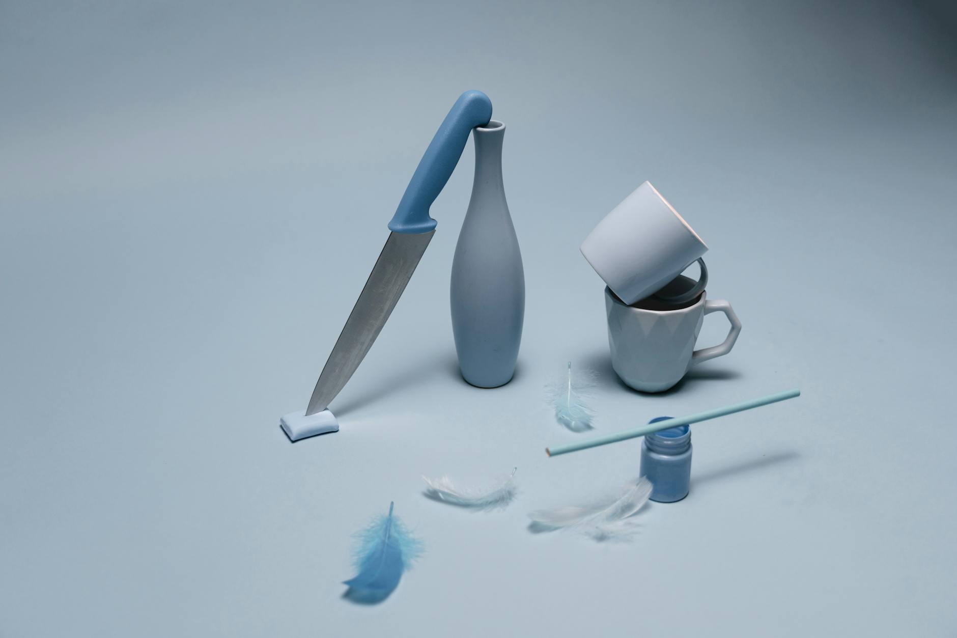A creative arrangement of blue ceramics, feathers, and a knife on a monochromatic background.