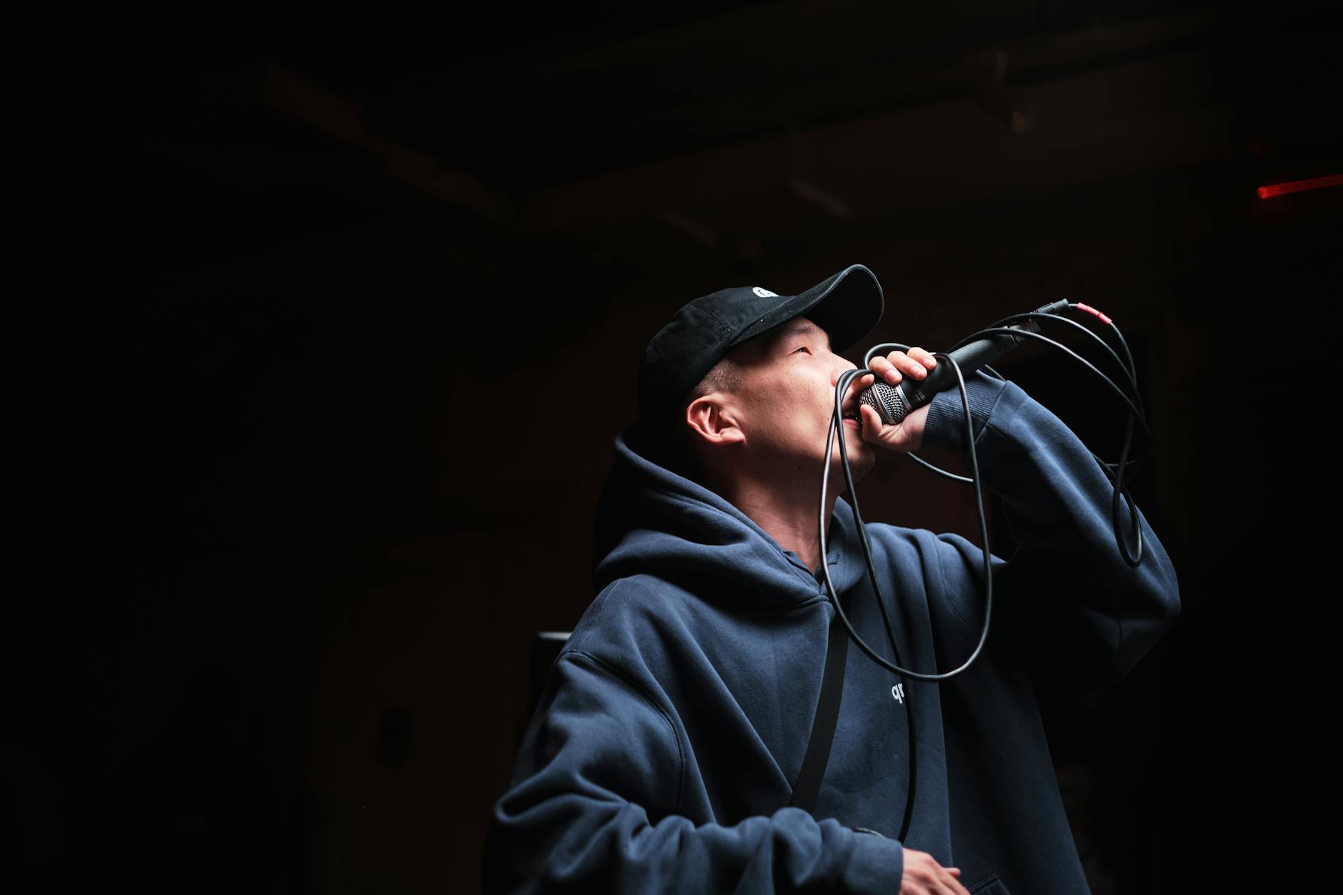 Dynamic shot of a male singer wearing a hoodie and cap, performing at a live concert with a microphone.