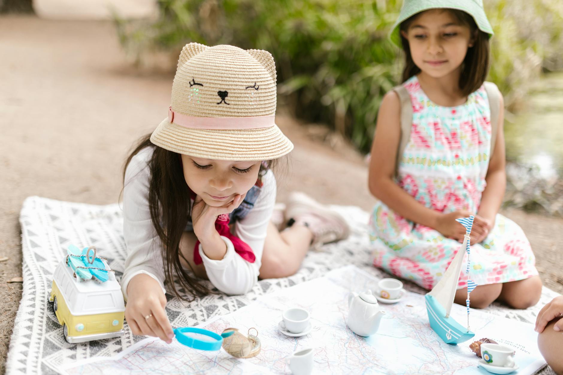 Two girls enjoying a playful outdoor picnic with toys and hats, embracing friendship and fun.