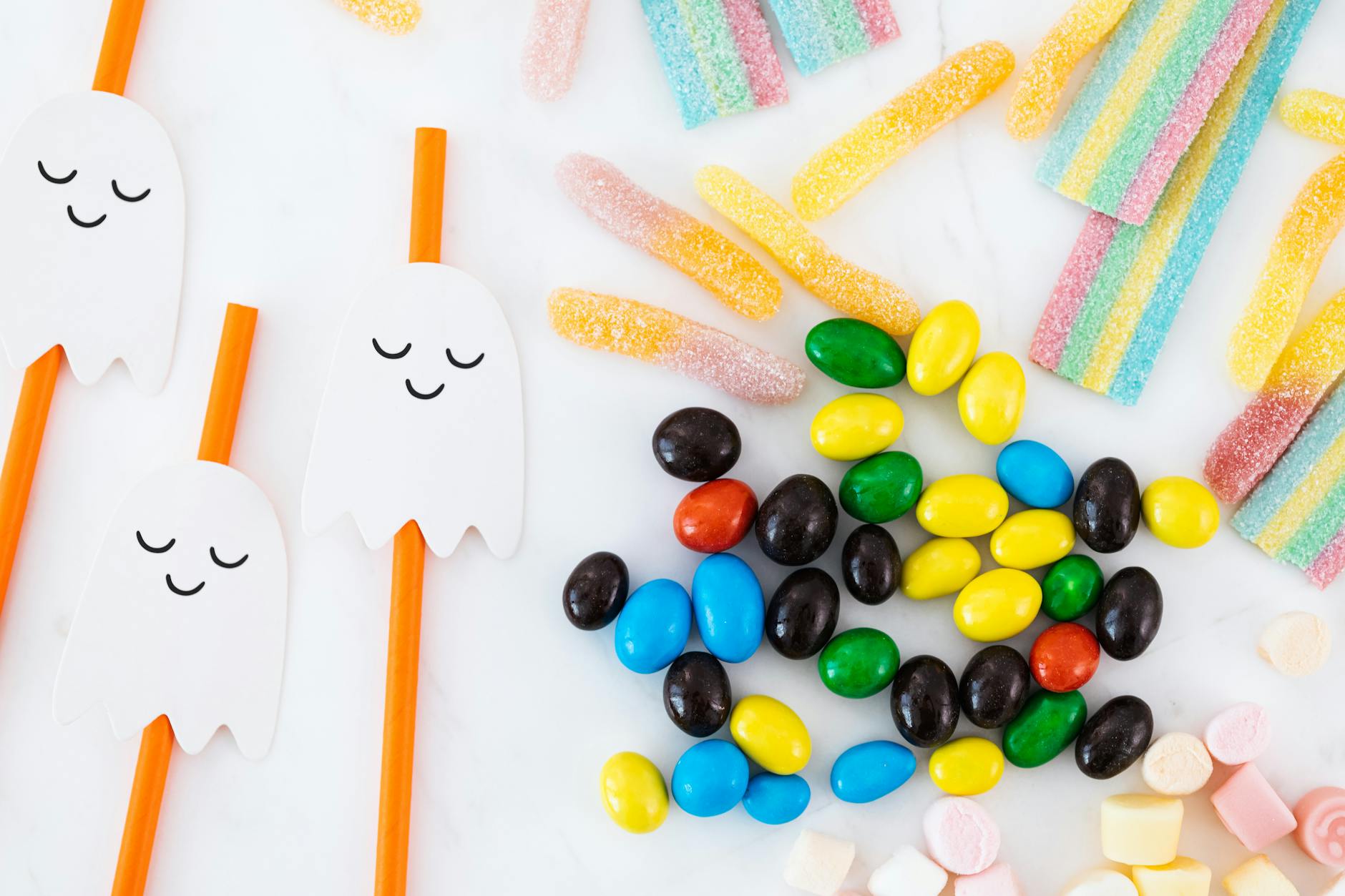 A festive flat lay of colorful Halloween candies and ghost decorations on a white background.