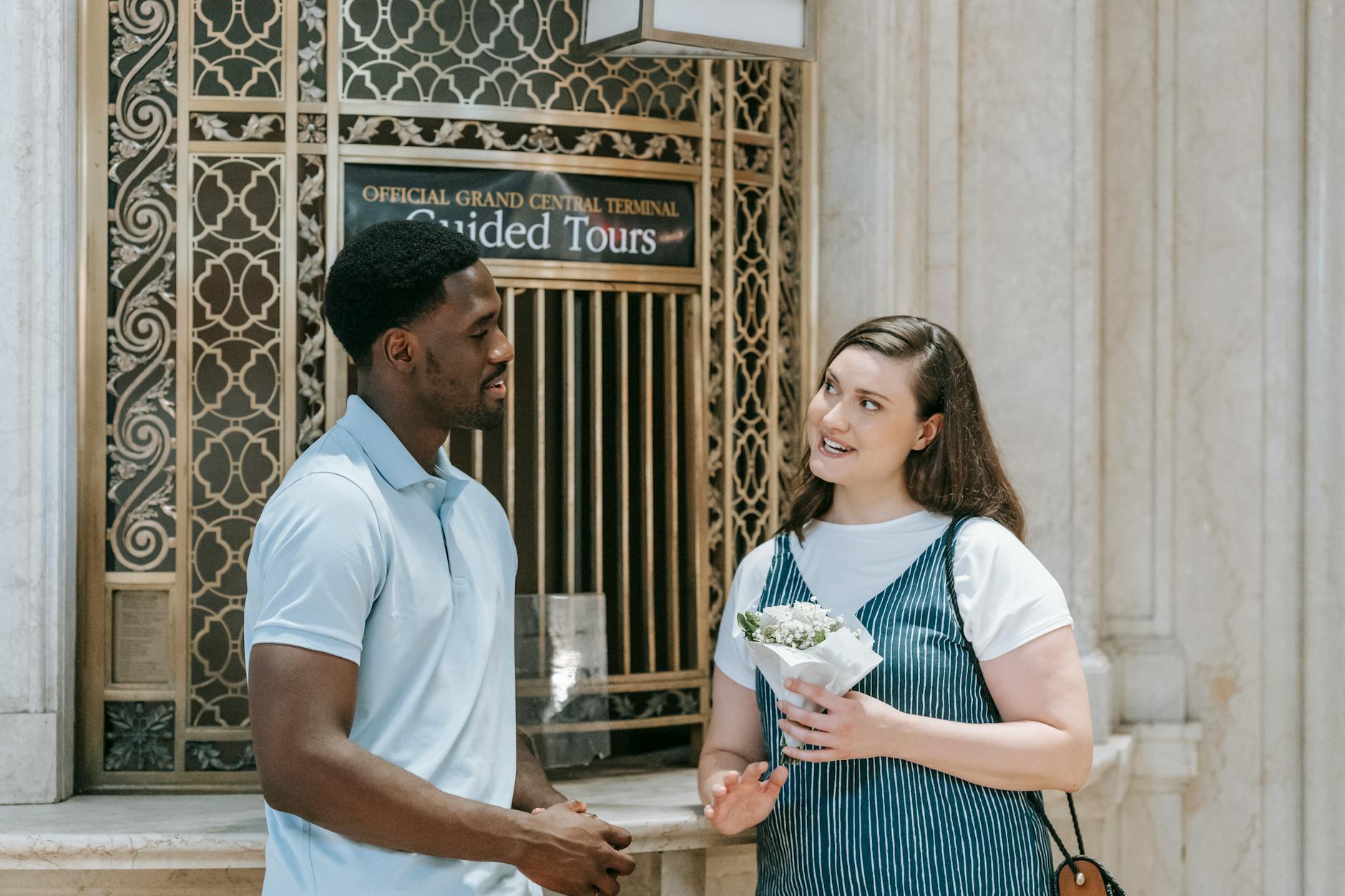 A diverse couple shares a conversation near Grand Central Terminal holding flowers, creating a vibrant urban scene.