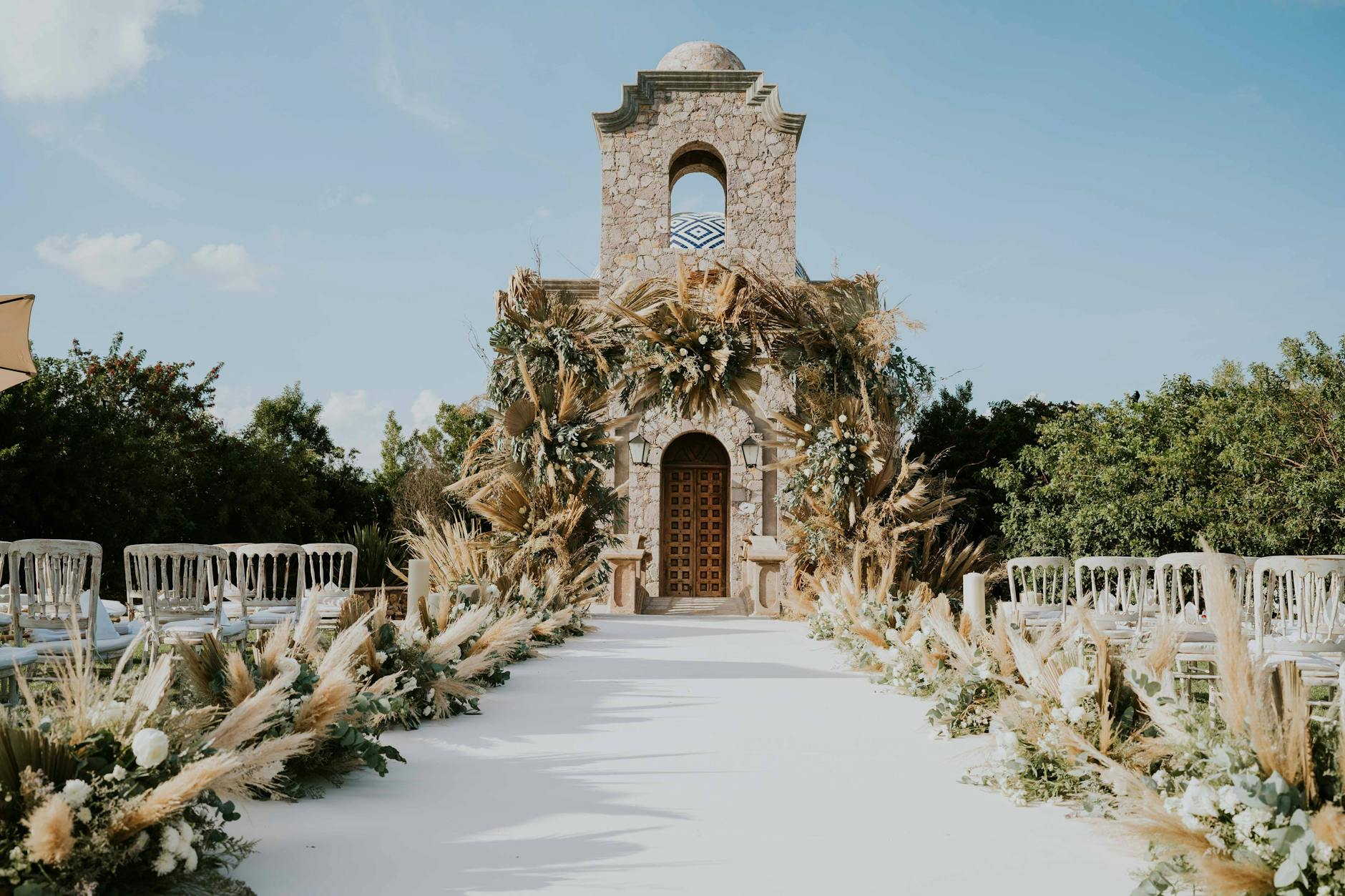 Beautiful outdoor wedding aisle with floral decorations leading to a stone building under a clear sky.