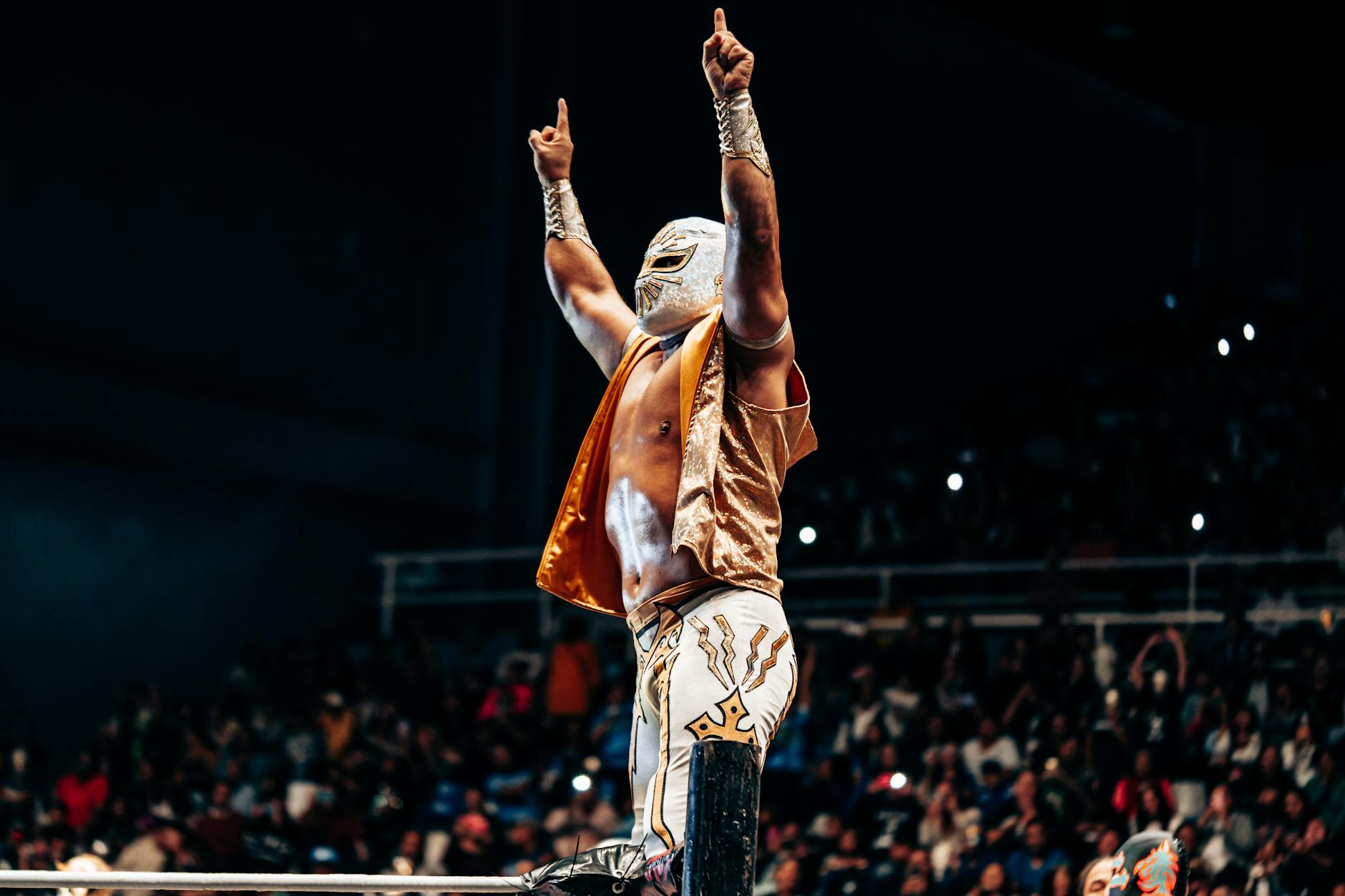 Masked wrestler celebrating victory in a vibrant Mexican wrestling arena.