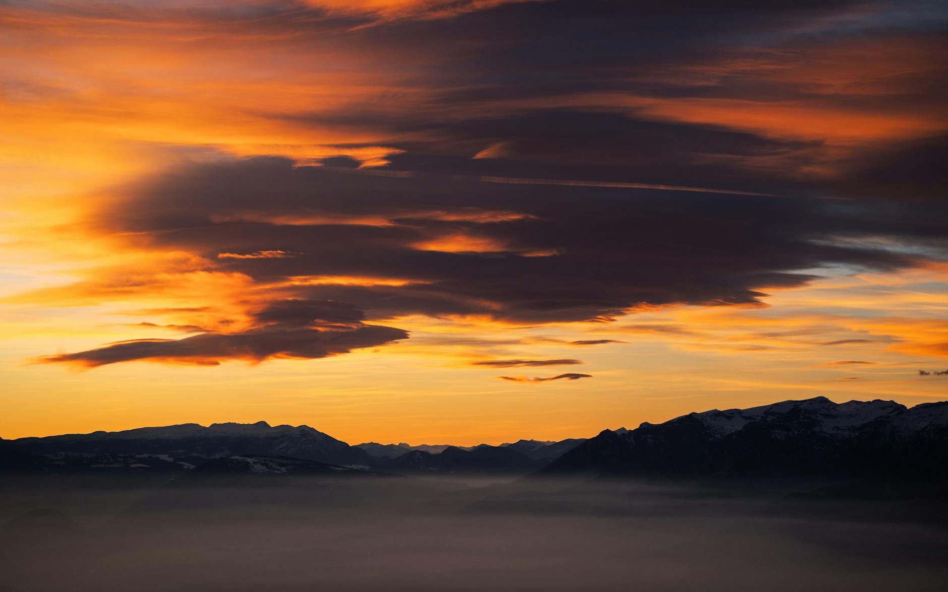 Dramatic sunset with vibrant clouds over misty mountains, capturing nature's beauty.