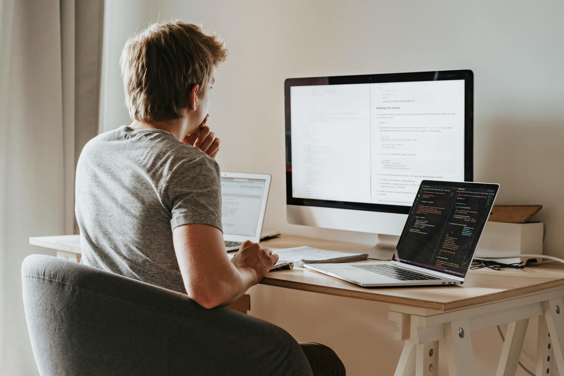 A man deeply engaged in software development with two laptops and a desktop monitor.