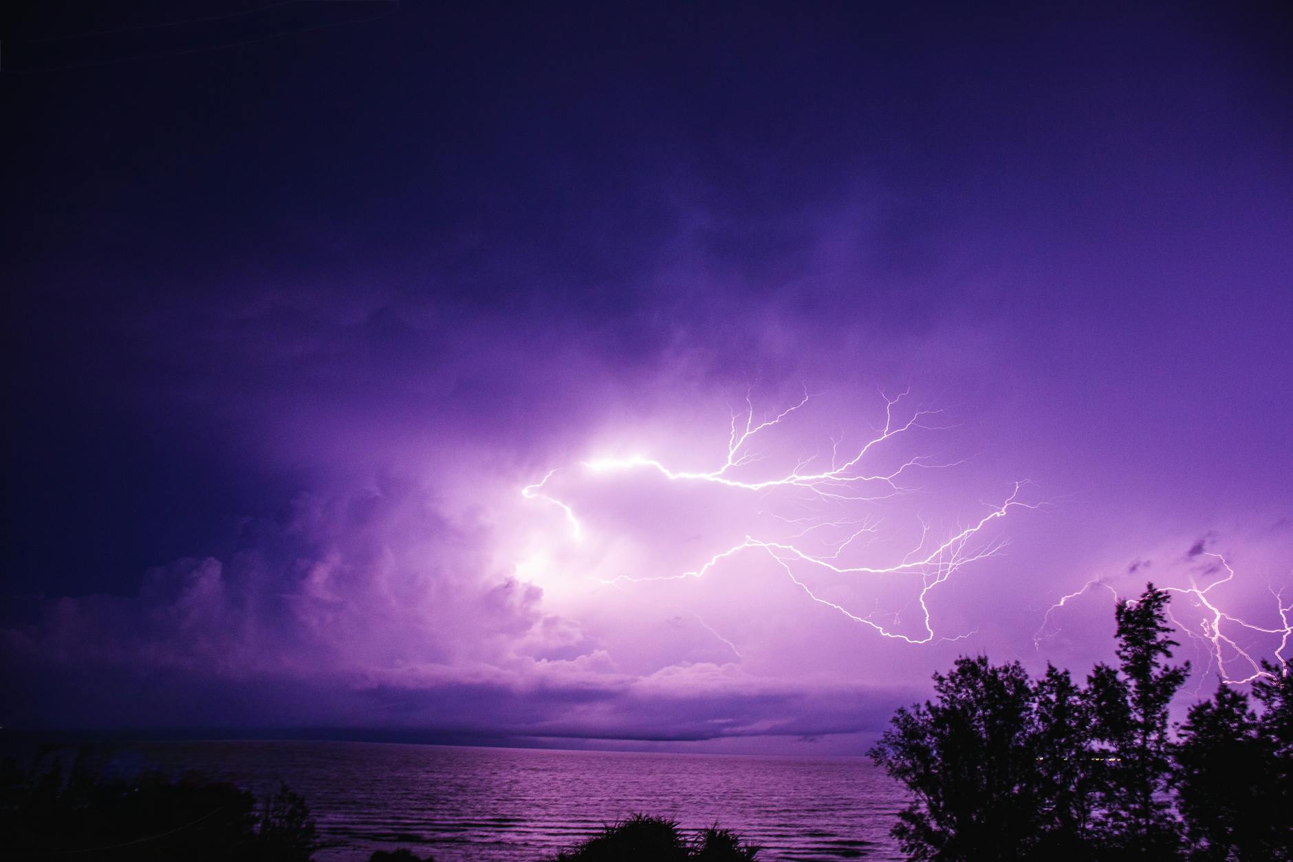 Dramatic purple lightning illuminating the night sky over the ocean, showcasing nature's power.