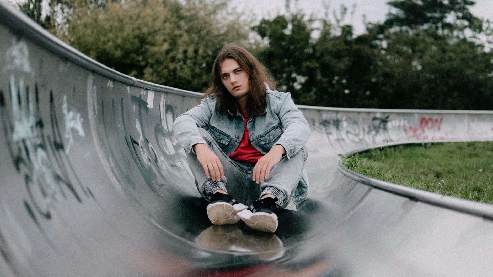 Young adult sitting on a graffiti skate ramp in Lodz, Poland, exuding a relaxed and modern vibe.