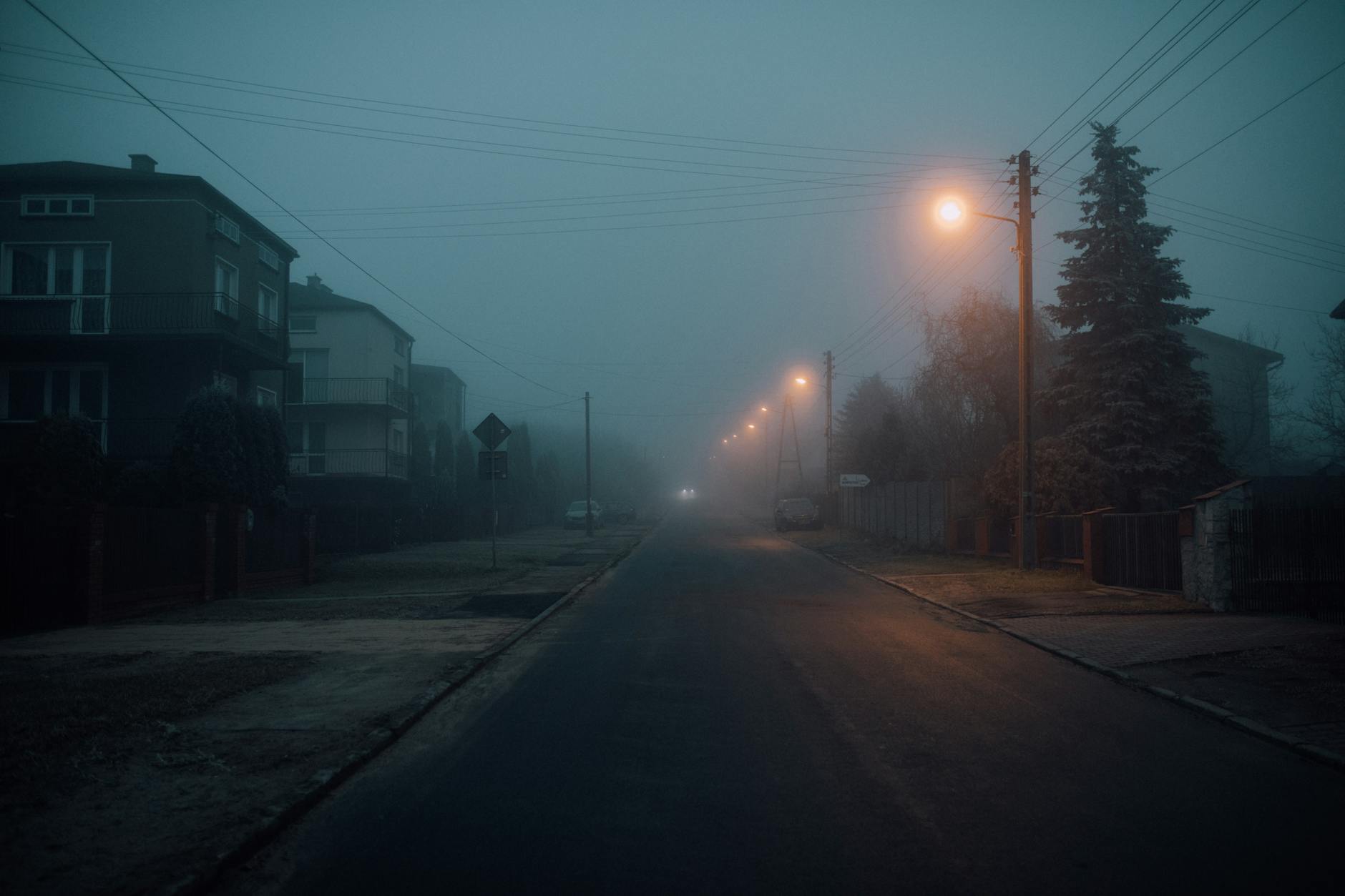 Misty night scene on a deserted road with glowing streetlights, capturing a moody atmosphere.