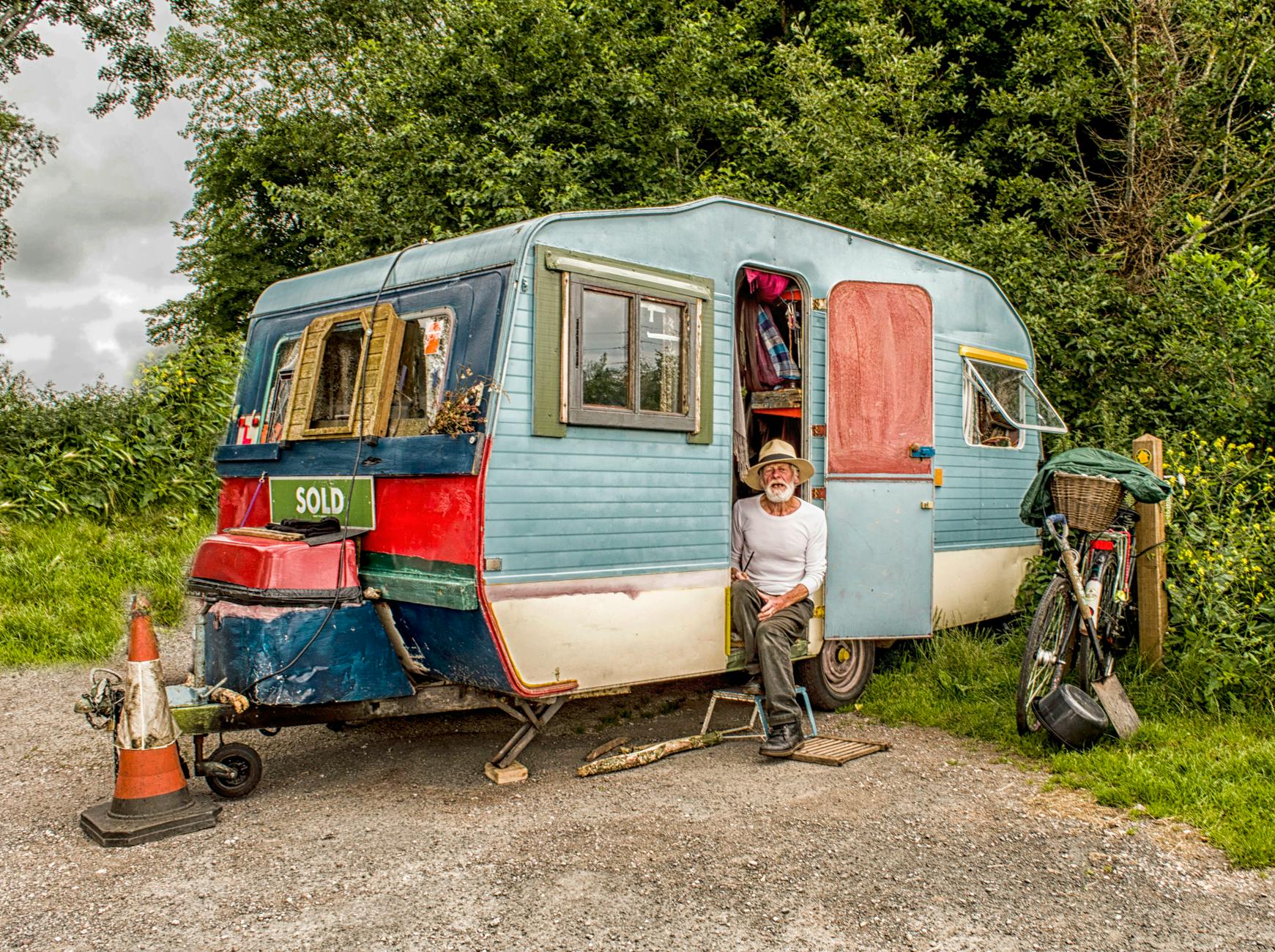 Vintage caravan with elderly man outdoors in Devon, showcasing rustic lifestyle and travel.