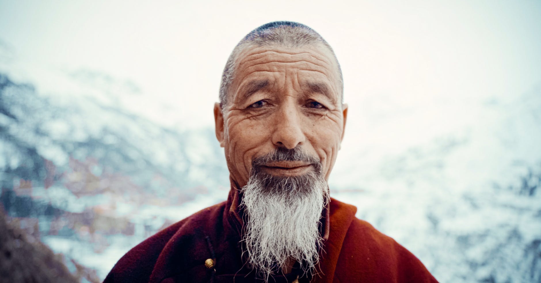 Elderly man with gray beard posing outdoors in snowy Manali.