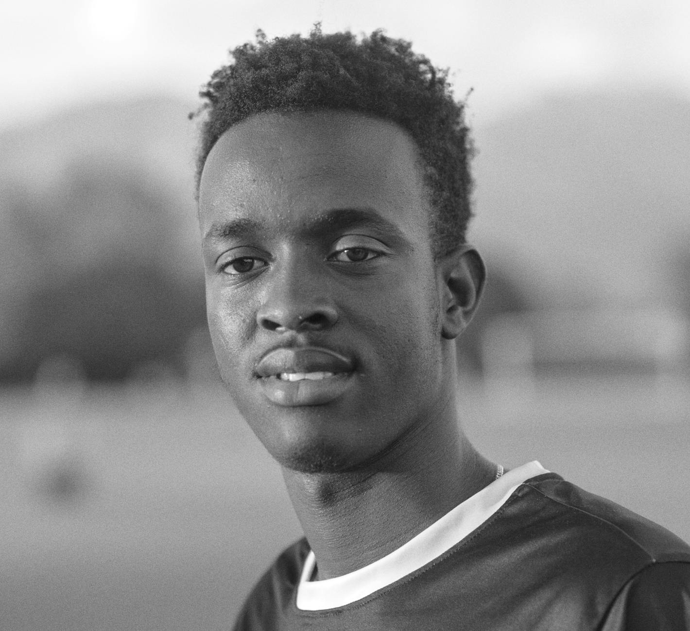 Artistic black and white portrait of a young male soccer player on an outdoor field.