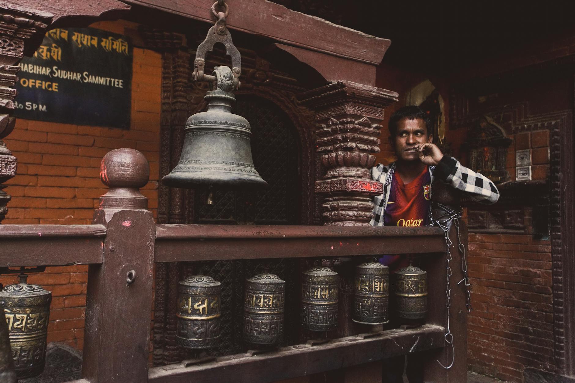 A man stands by traditional prayer bells at a historical structure, showcasing cultural heritage.