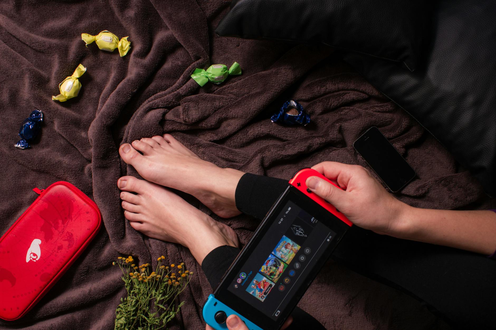 Close-up of a person playing Nintendo Switch with candy and a cozy blanket.