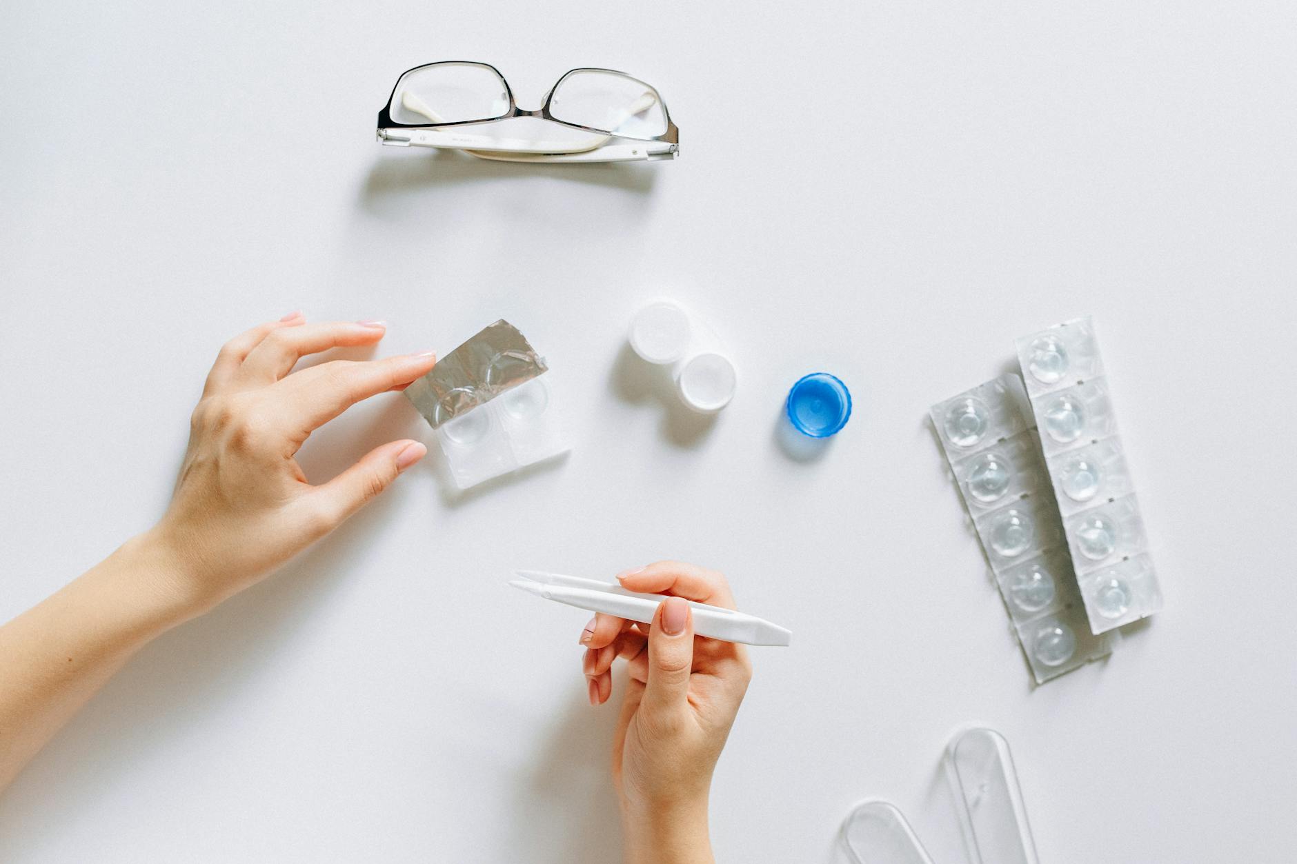 Flat lay setup of contact lenses with eyeglasses for eye care on a white background.