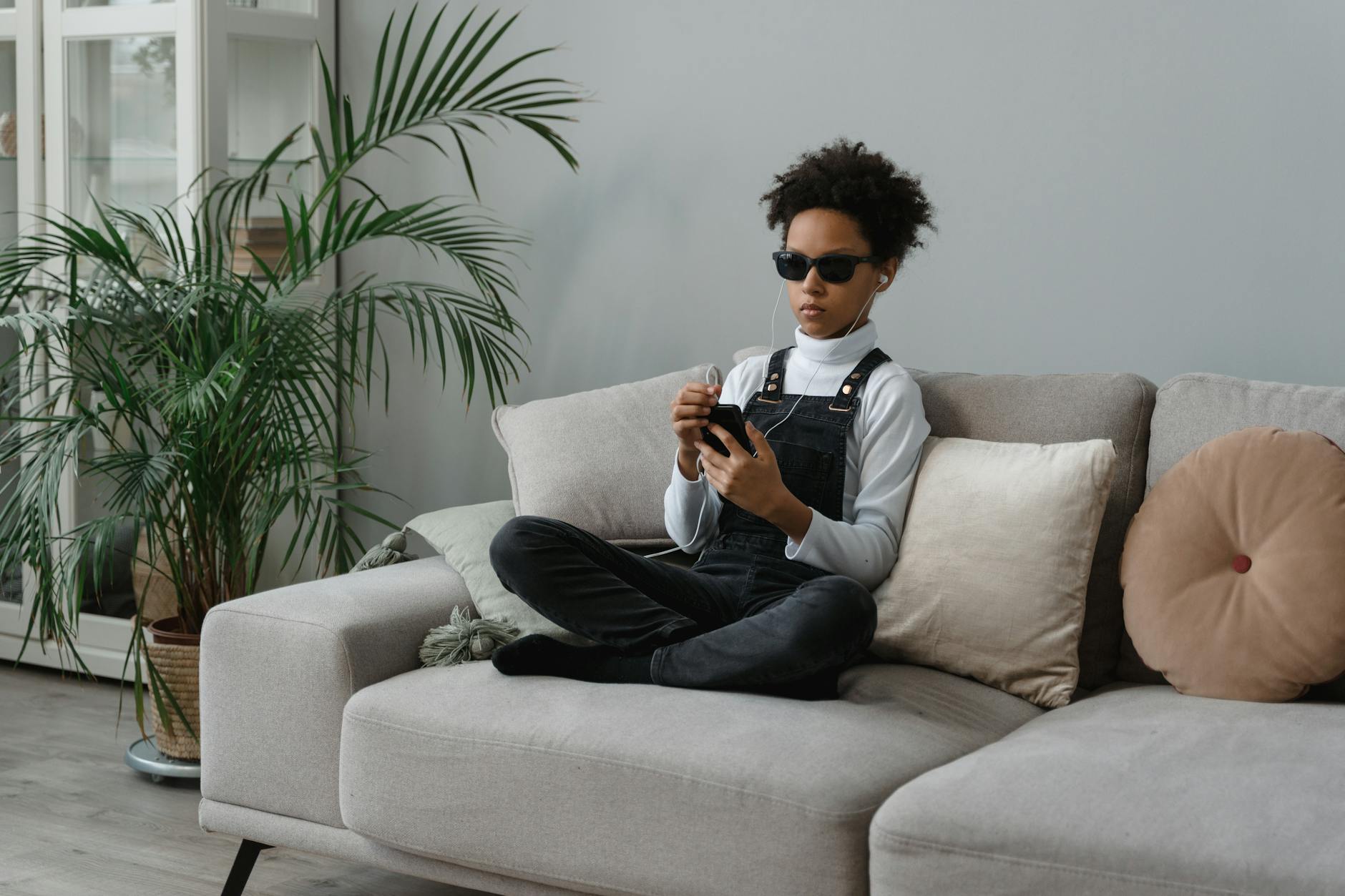 A visually impaired teenager sitting on a sofa using a smartphone and headphones.