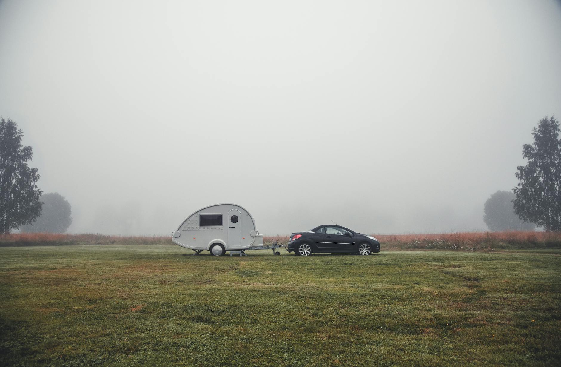 Car with a trailer in a foggy field captures serene morning in Dalarna County, Sweden.