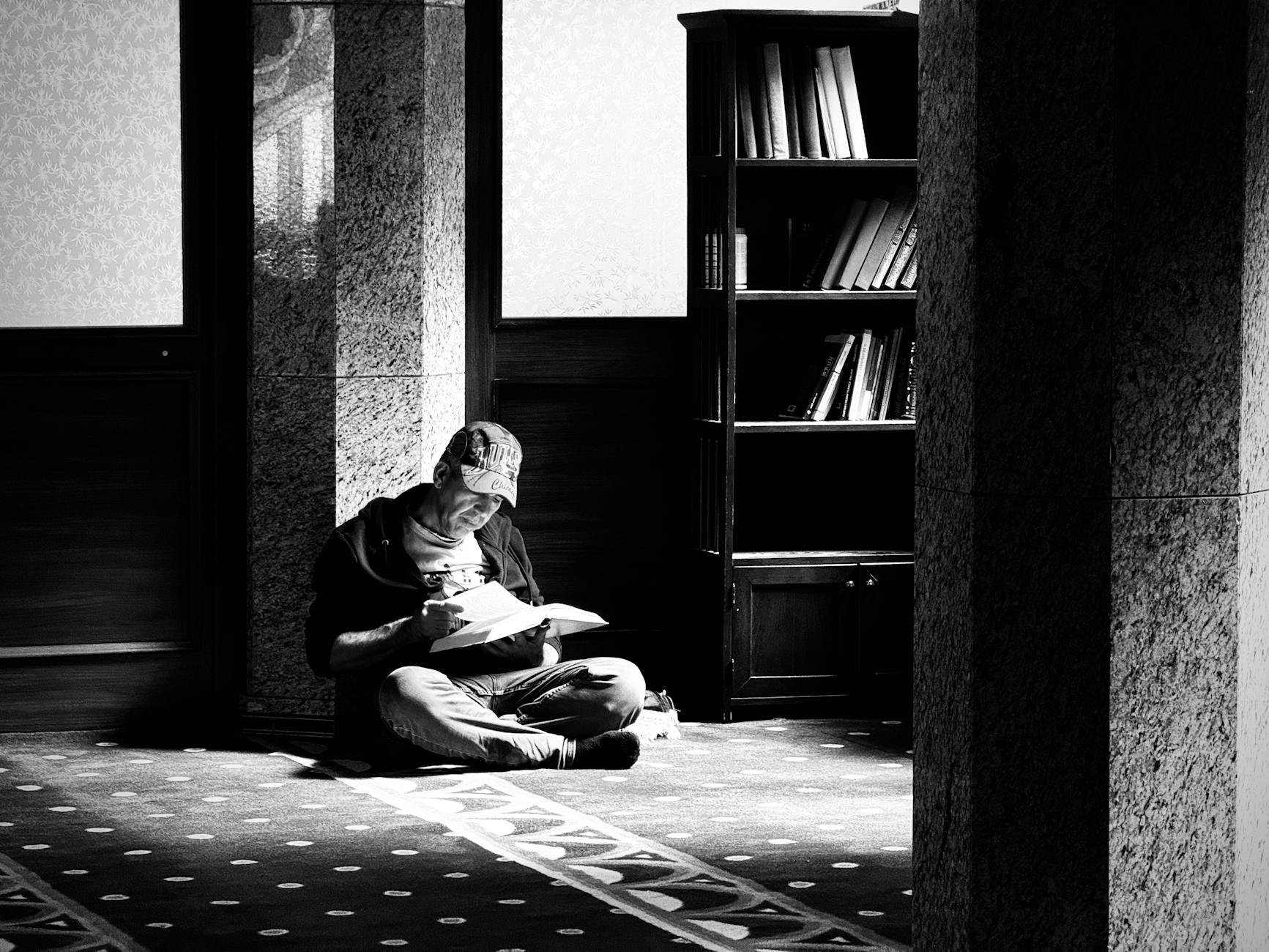 A contemplative scene of a man reading inside a mosque in Ankara, Türkiye, captured in black and white.