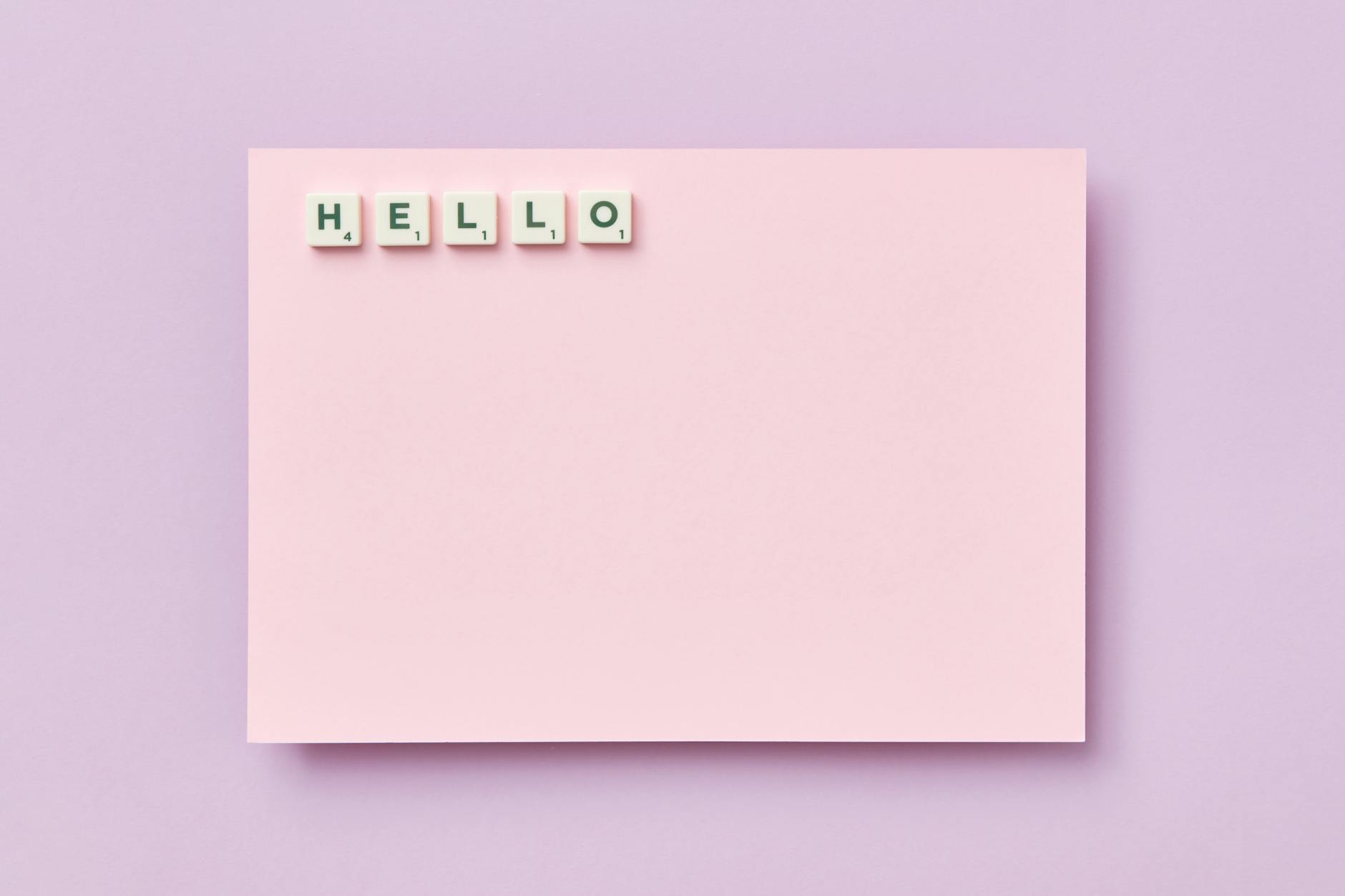 Pink card featuring the word 'Hello' spelled with Scrabble tiles on a pastel background.