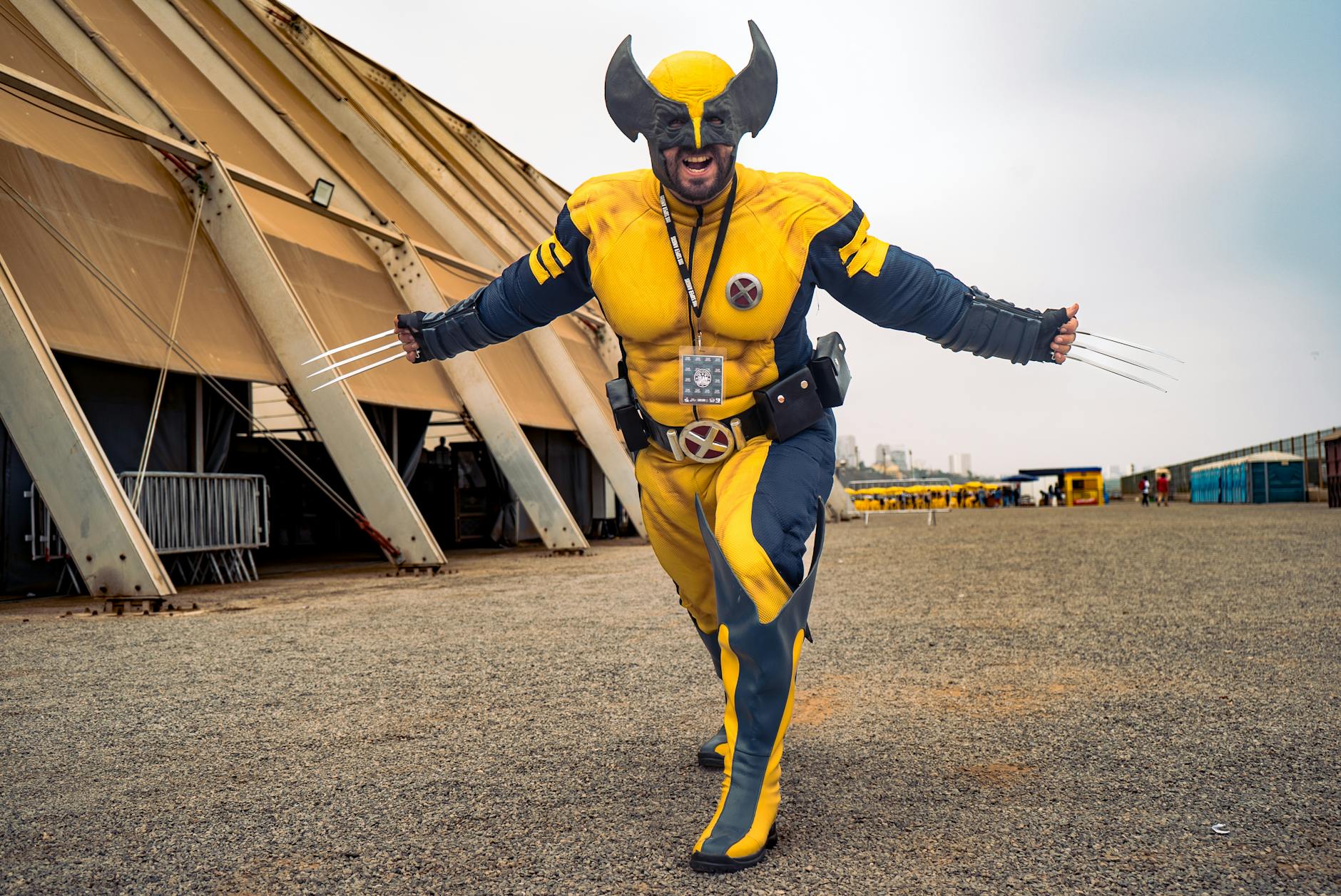 A cosplayer vividly dressed as Wolverine with claws extended outdoors showing excitement.