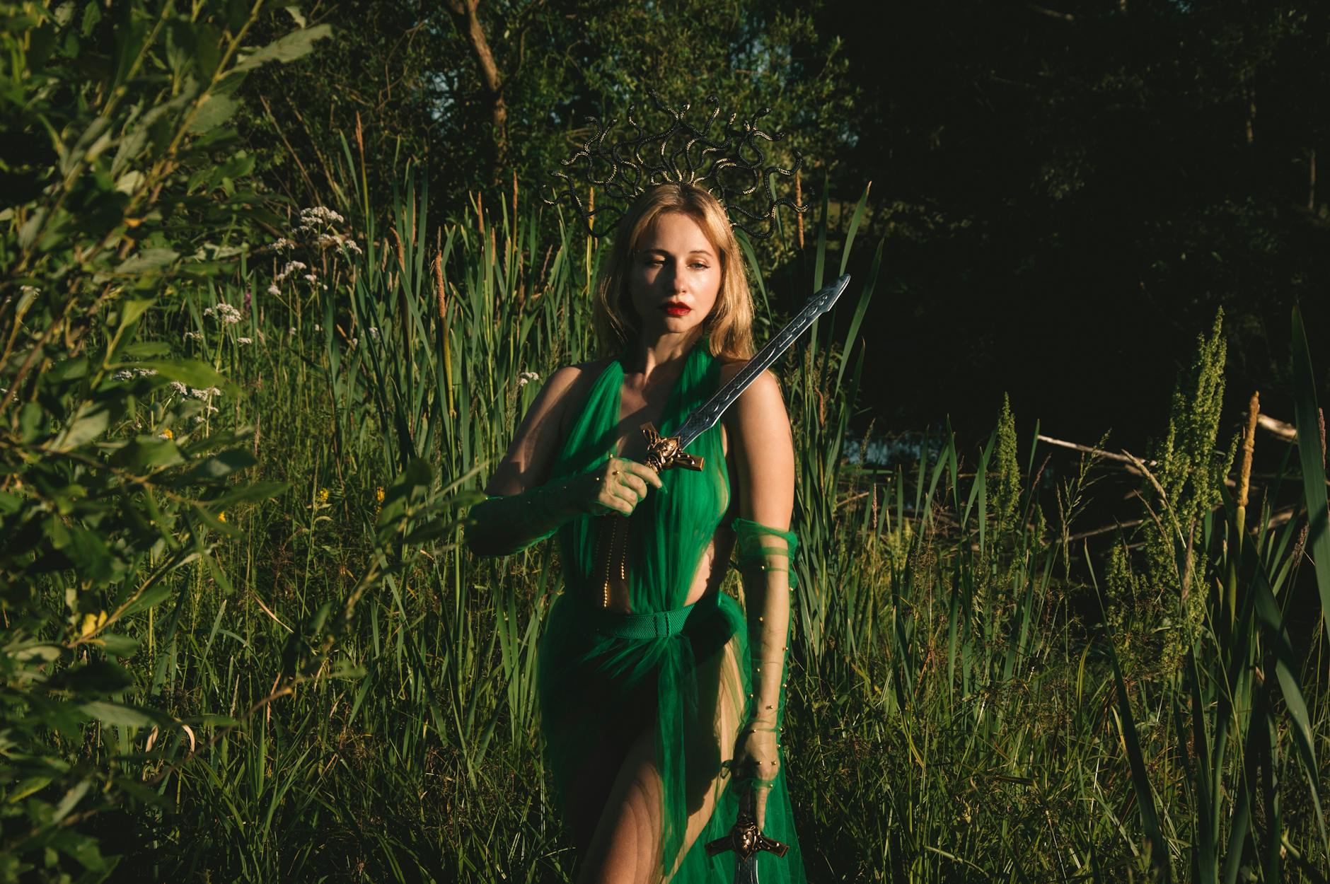 A woman in a green dress holds a sword in a mystical forest setting, evoking fantasy themes.