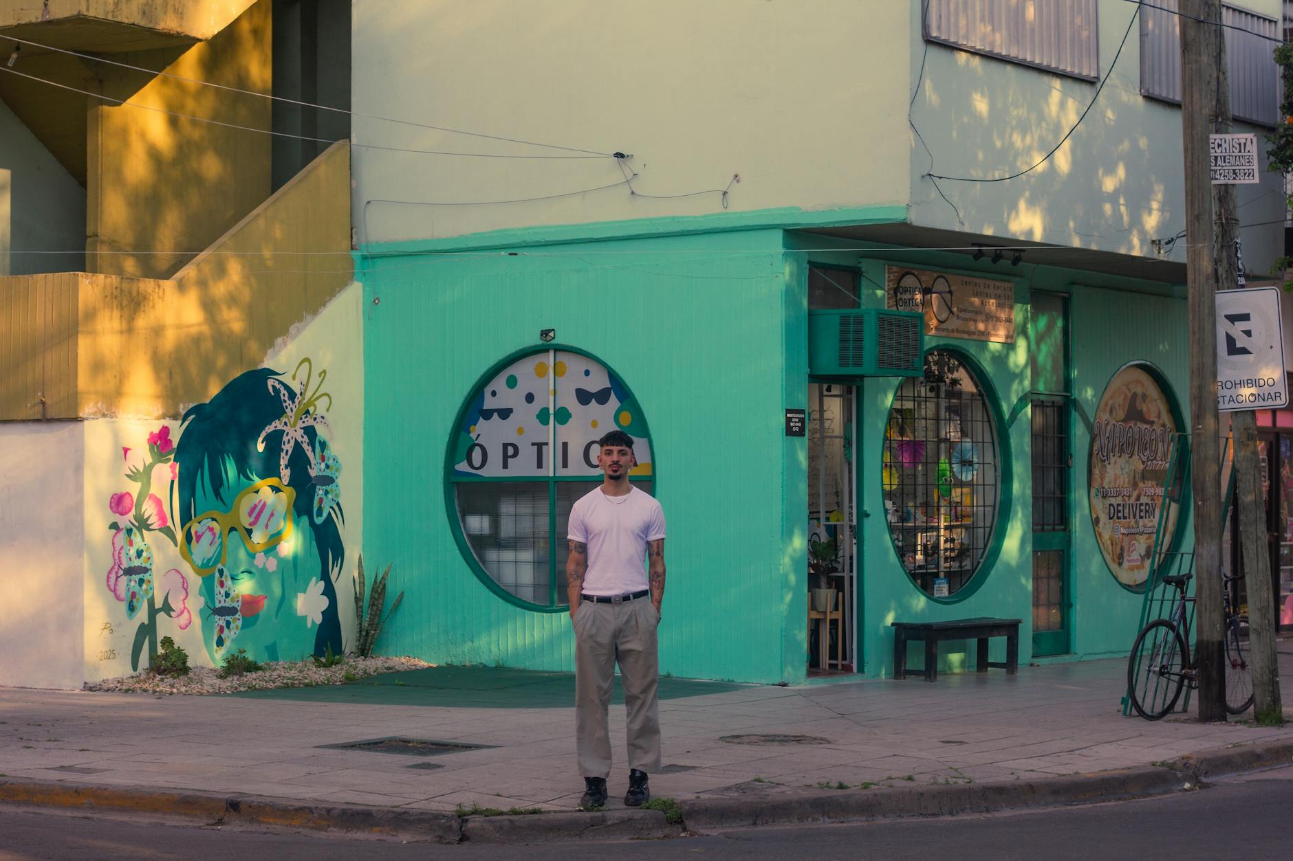 A man stands in front of a vibrant mural on a sunny street in Argentina.