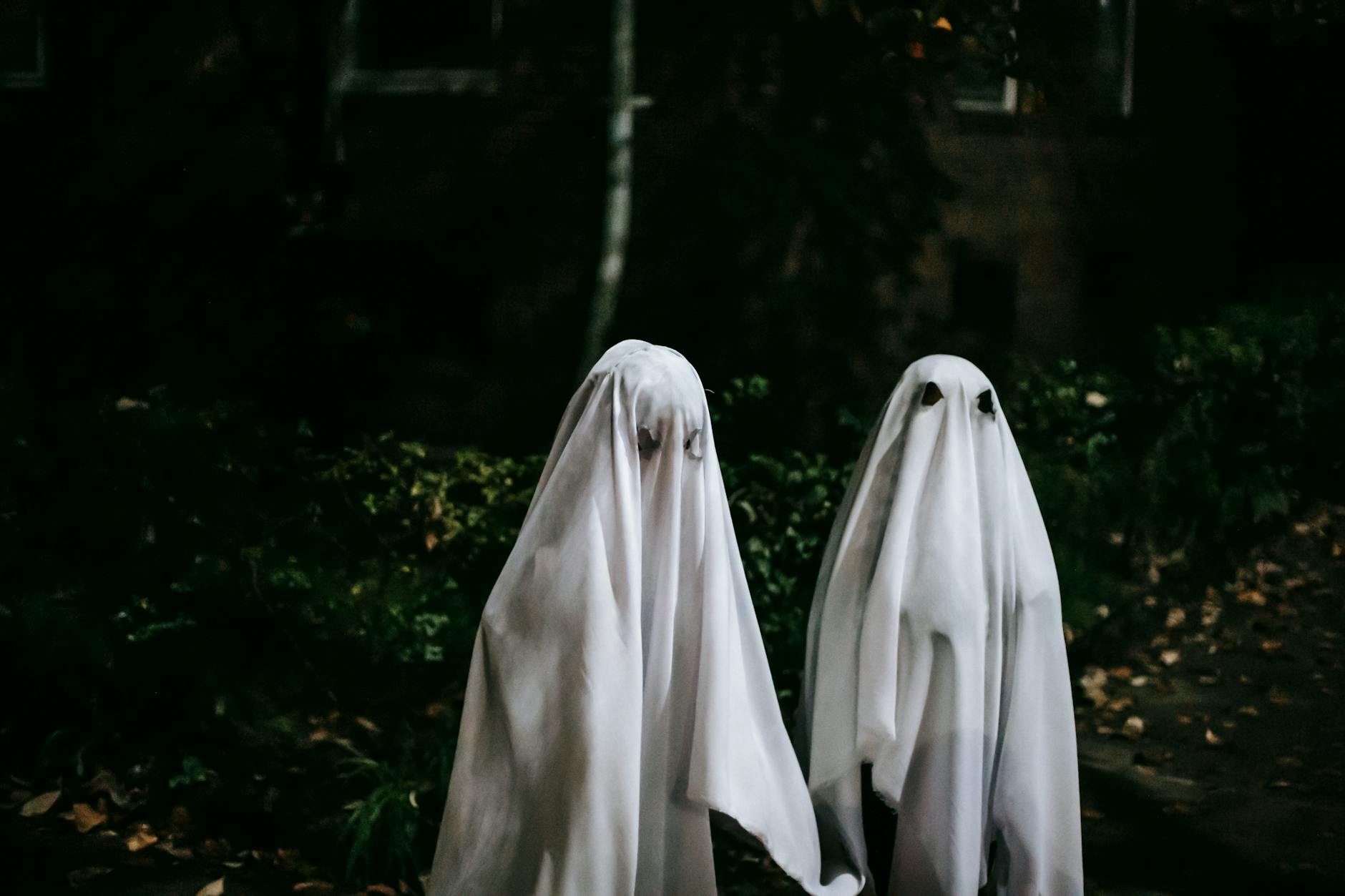 Anonymous friends in phantom costumes with holes for eyes spending time together on Halloween night in city