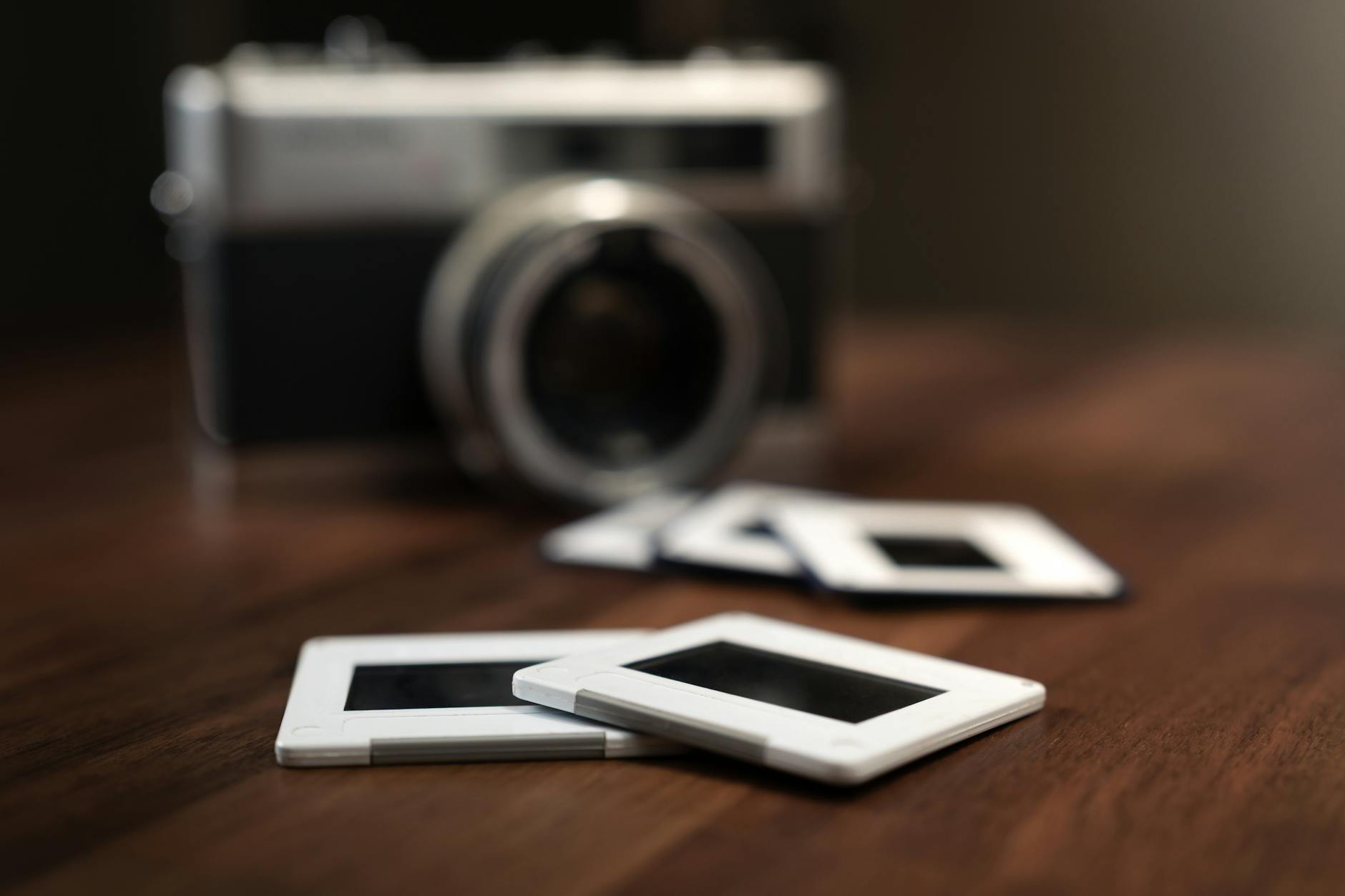 Several photo slides resting on a wooden table, accompanied by a vintage camera in the background, evoke nostalgic memories of past travels and cherished experiences