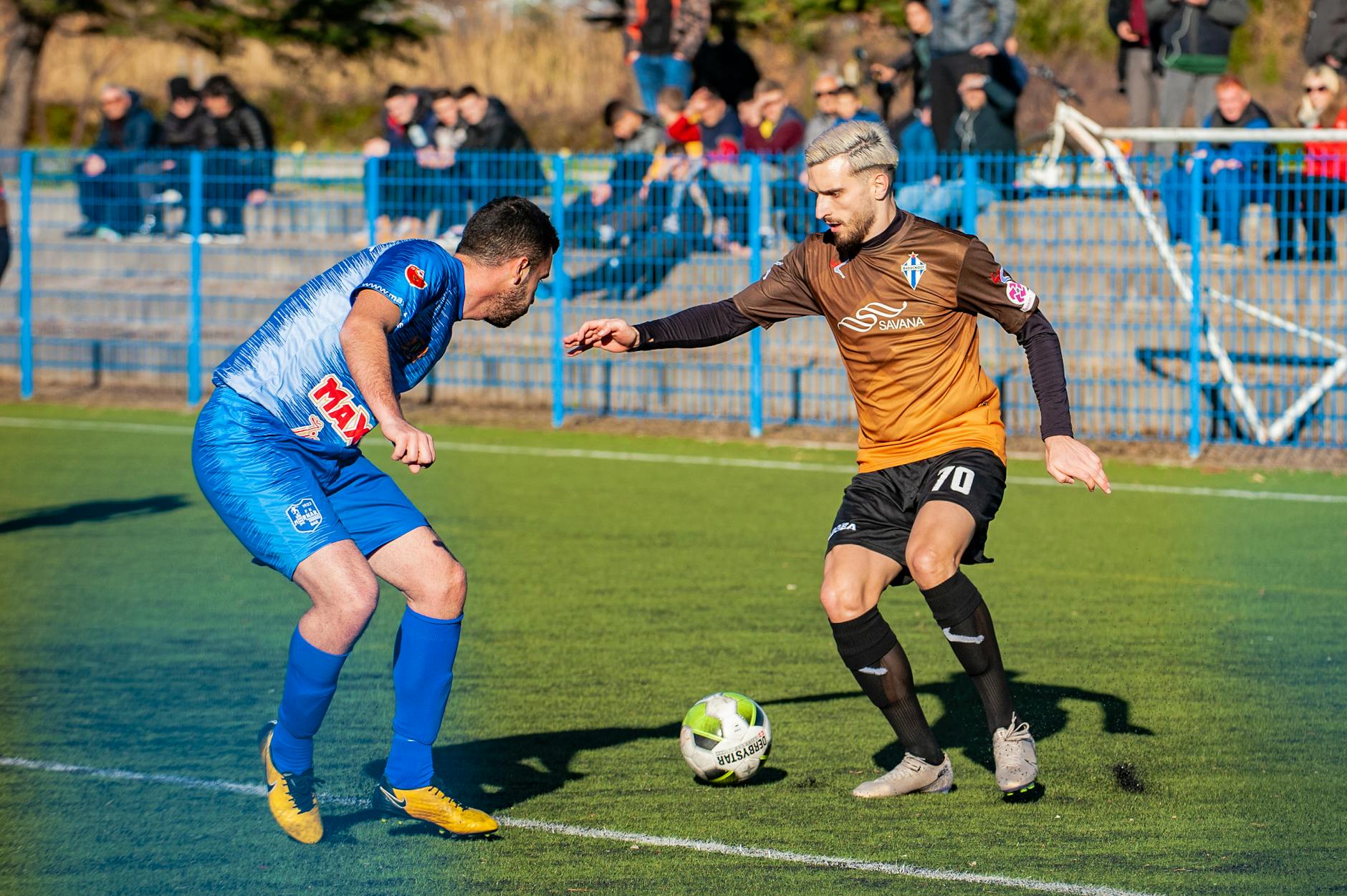 Two male soccer players in action during a competitive match on a grass field.