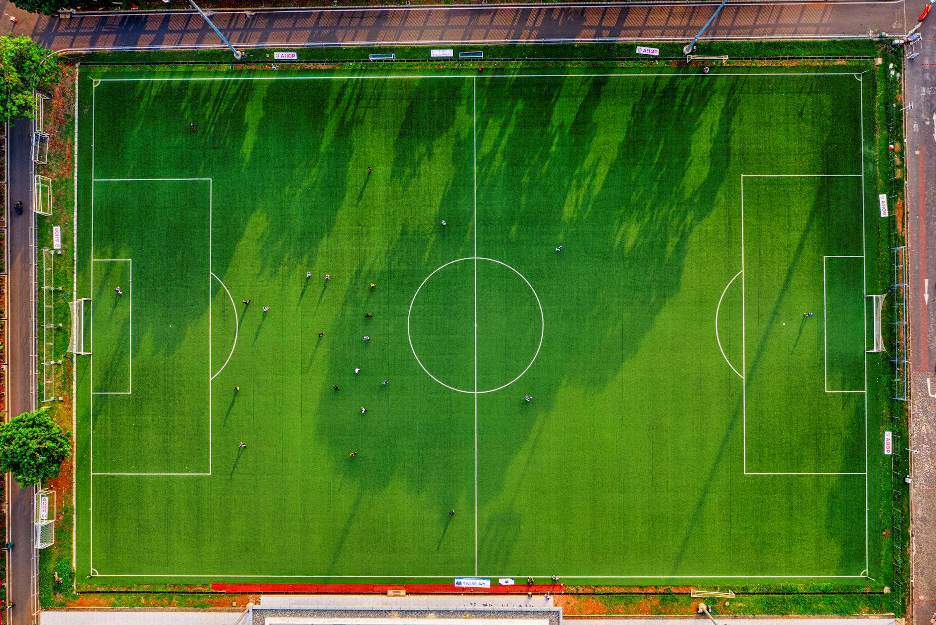 High-angle drone shot of a soccer field with players in Jakarta, Indonesia.