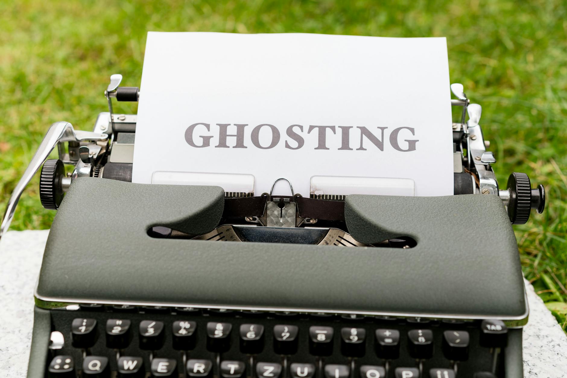 A vintage typewriter displaying the word 'Ghosting' on a white paper, set outdoors on grass.