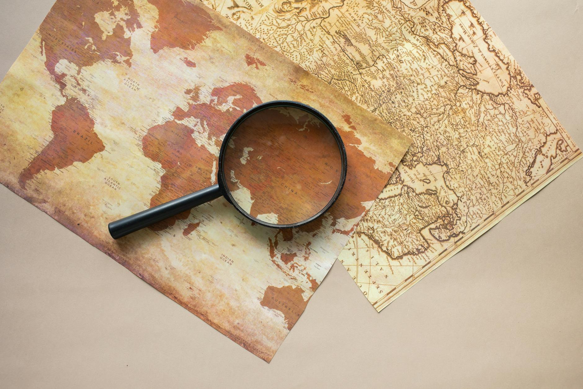 A vintage world map and magnifying glass on beige paper, ideal for exploration themes.