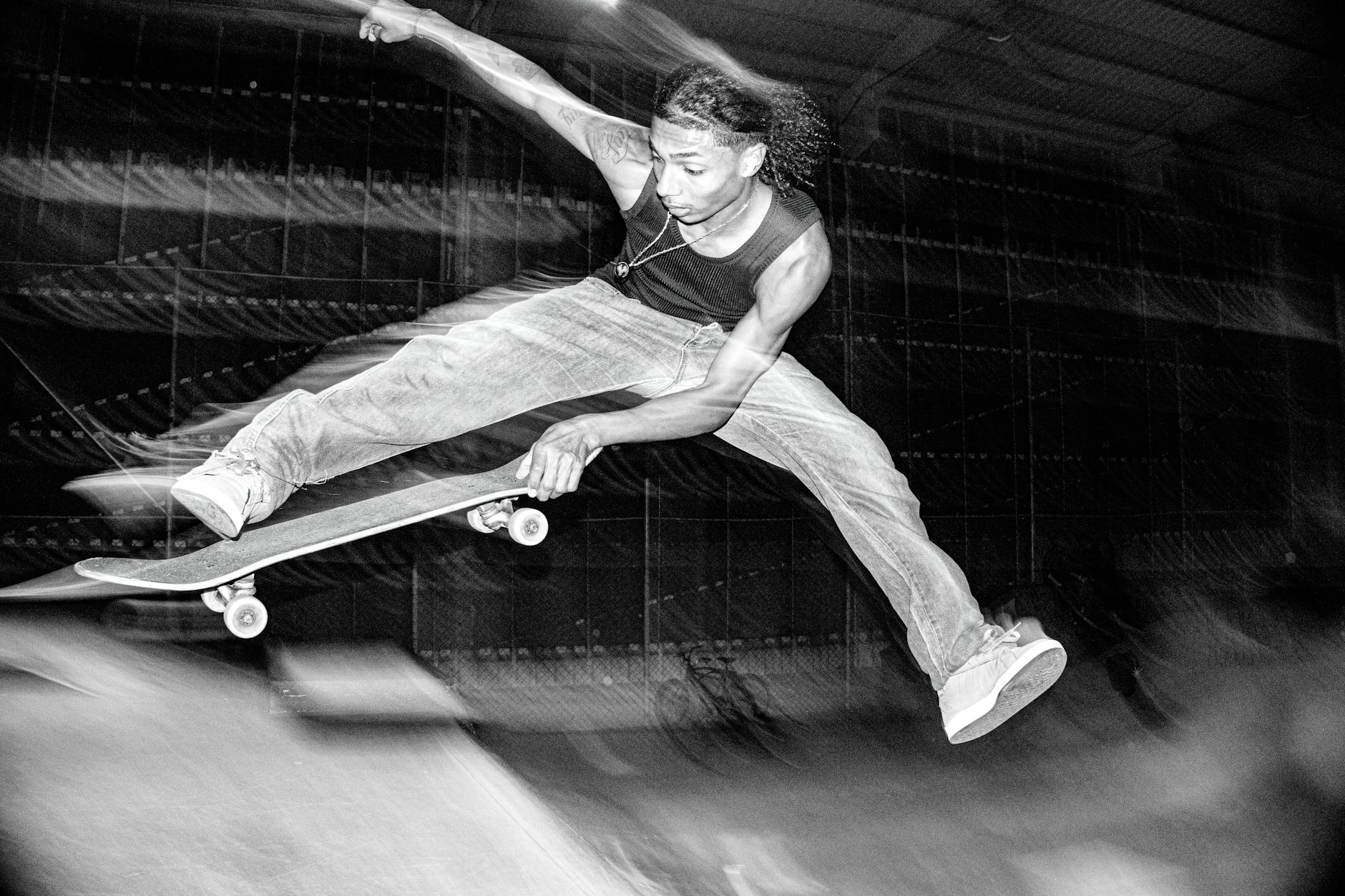 A skateboarder performs an aerial trick indoors in a high-energy black and white photo.