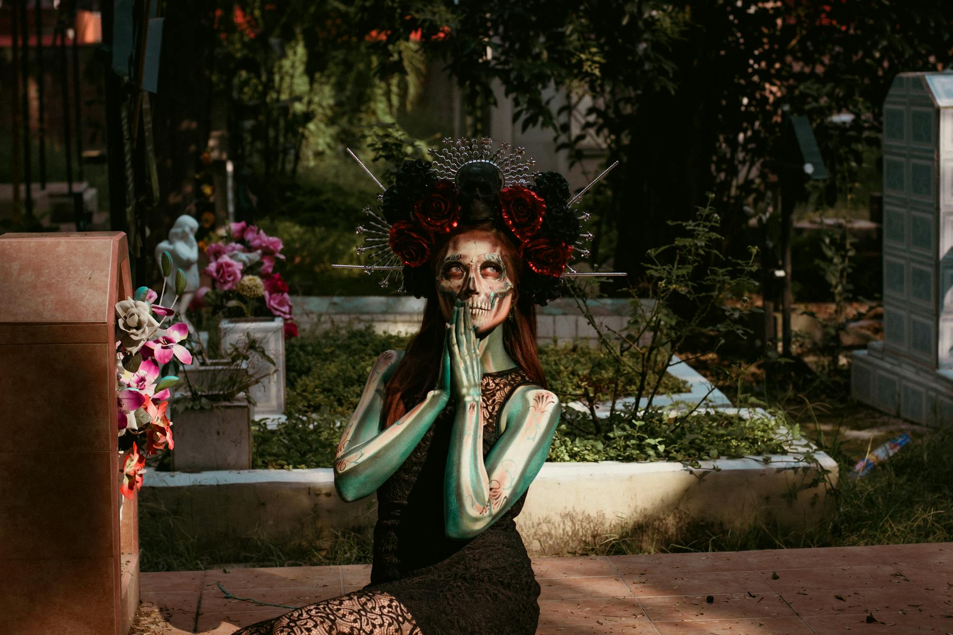 A woman with artistic makeup sits in a cemetery, embodying the spirit of Día de Muertos in Mexico.