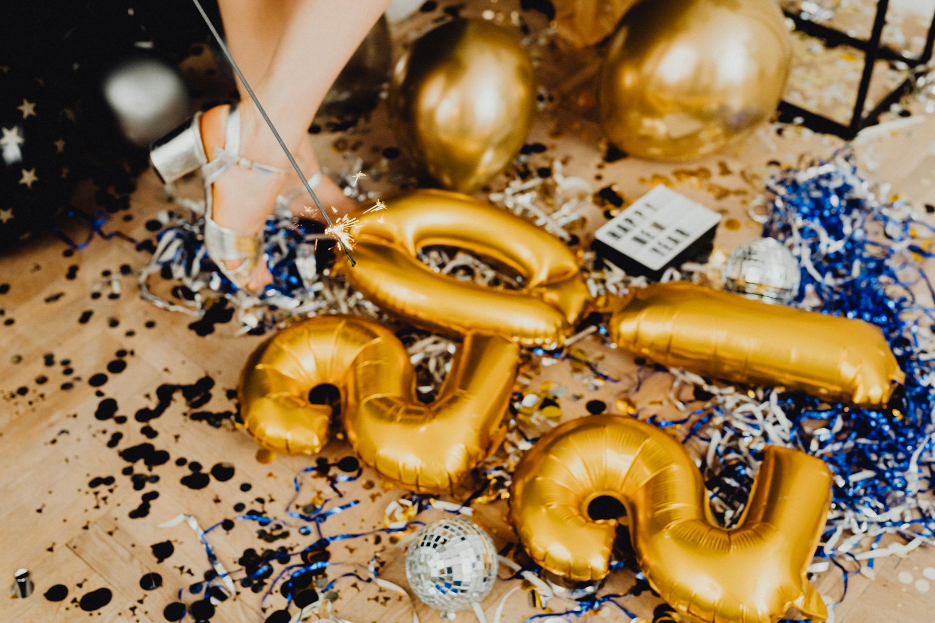 Festive floor with New Year balloons, tinsel, and a sparkler creating a vibrant party scene.