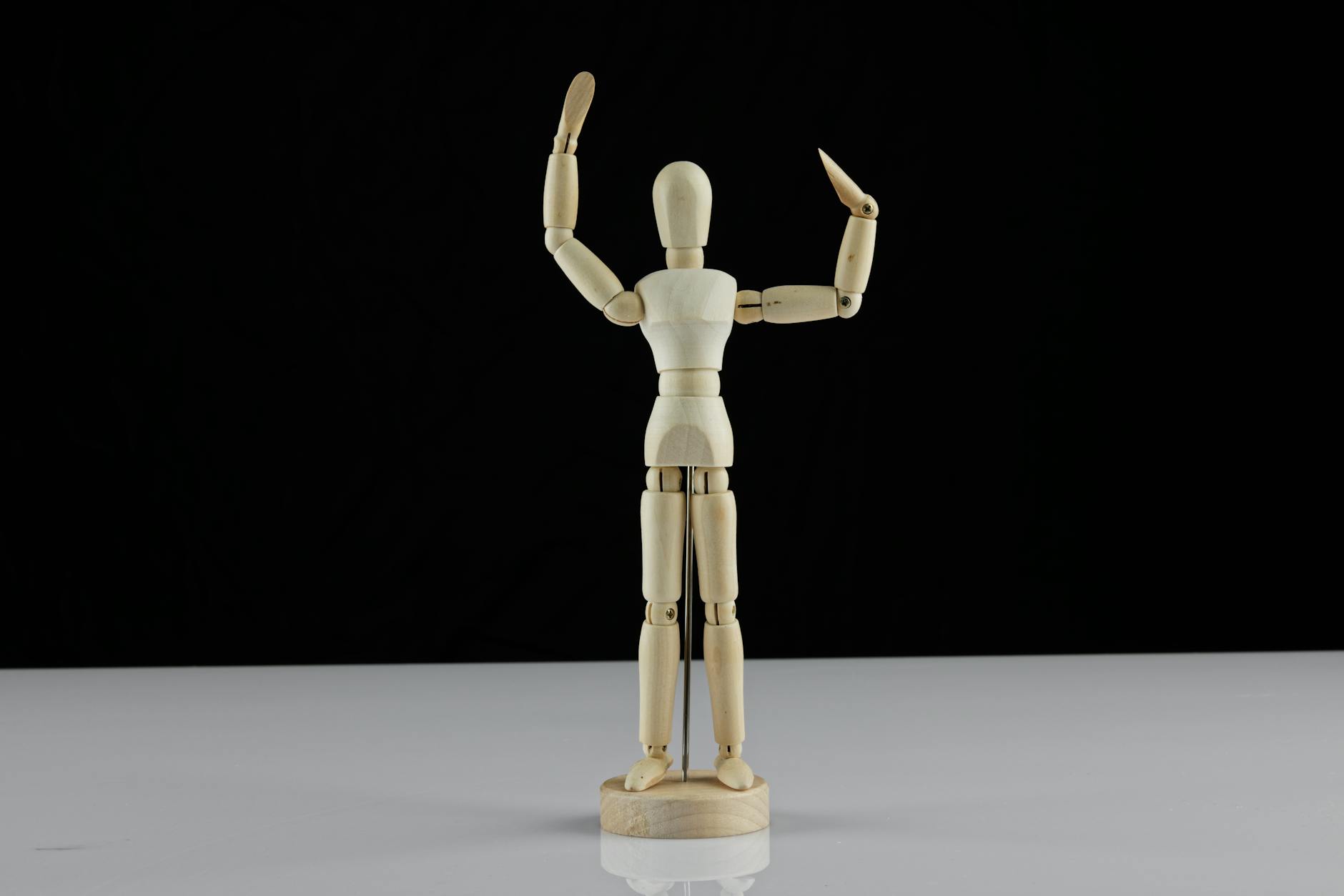 Wooden artist mannequin standing with arms raised on a black background, ideal for art and craft projects.