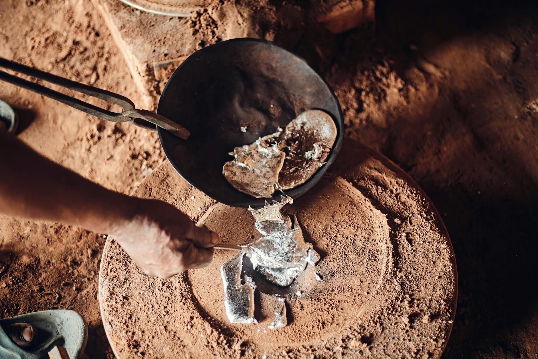 Hands working with molten metal in a traditional smelting process, showcasing craftsmanship.