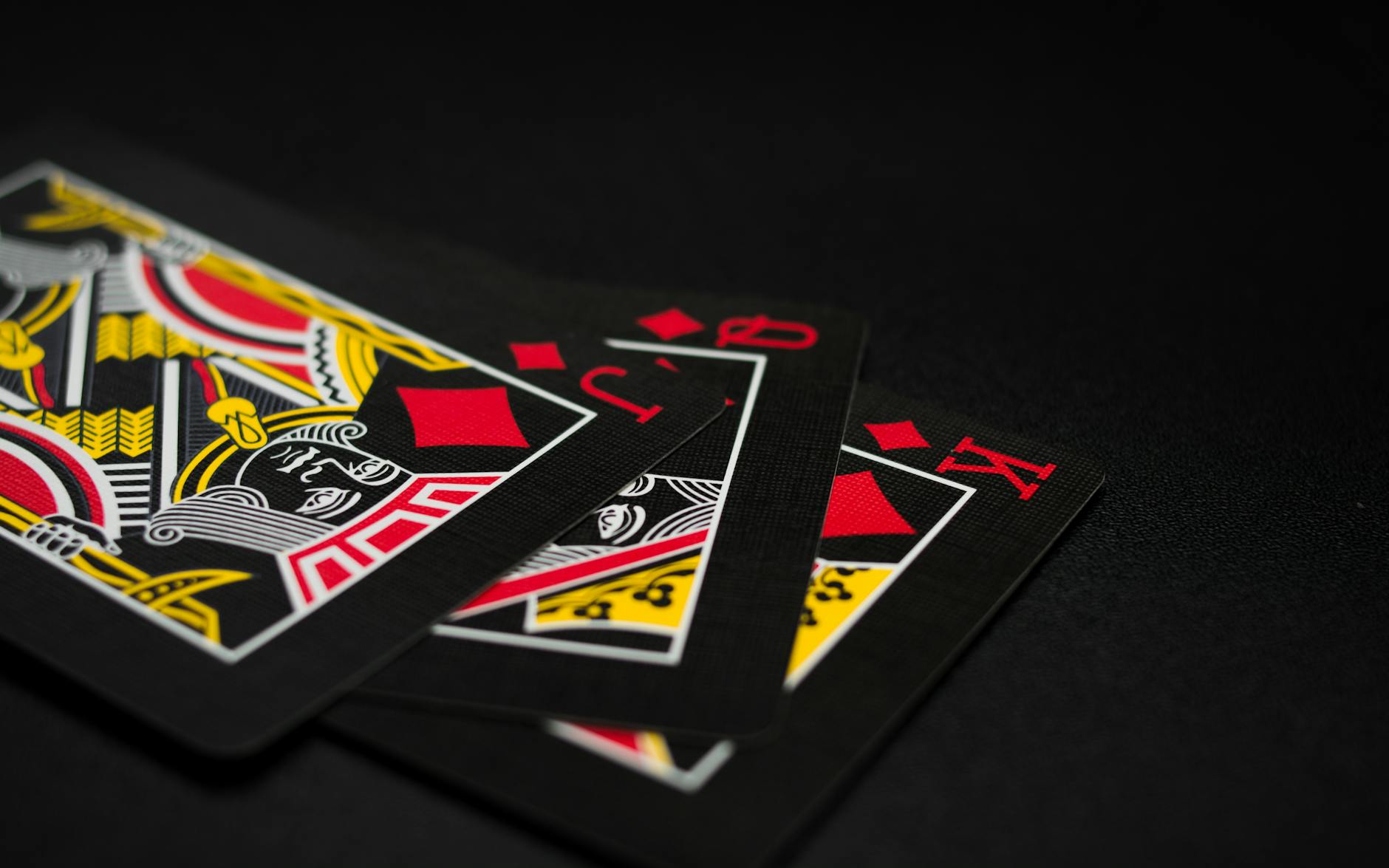 A close-up image of playing cards, highlighting King, Queen, Jack, Ace of Diamonds on dark background.